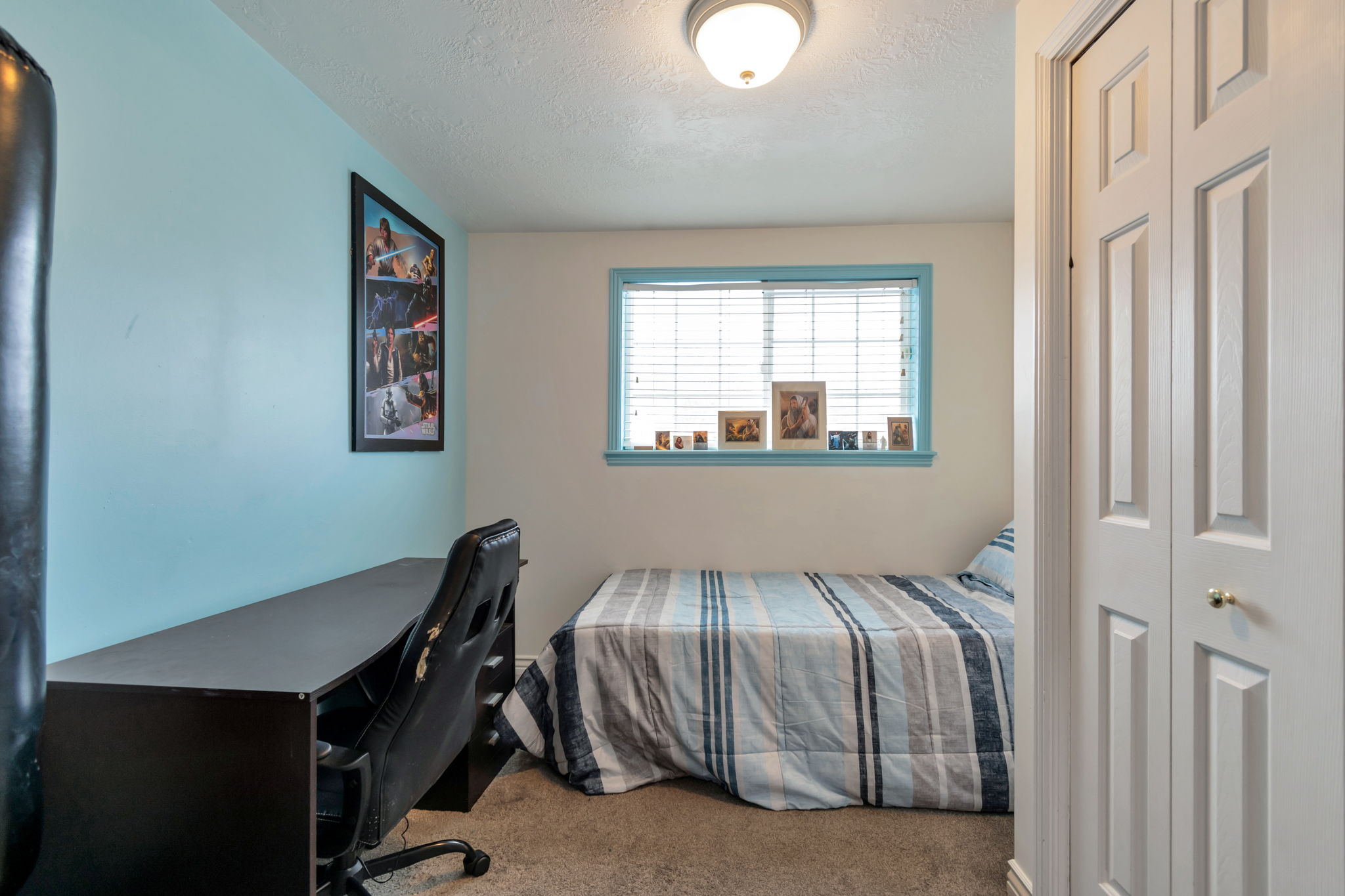 Bedroom featuring light blue accent wall, neutral carpeting, and a window with horizontal blinds