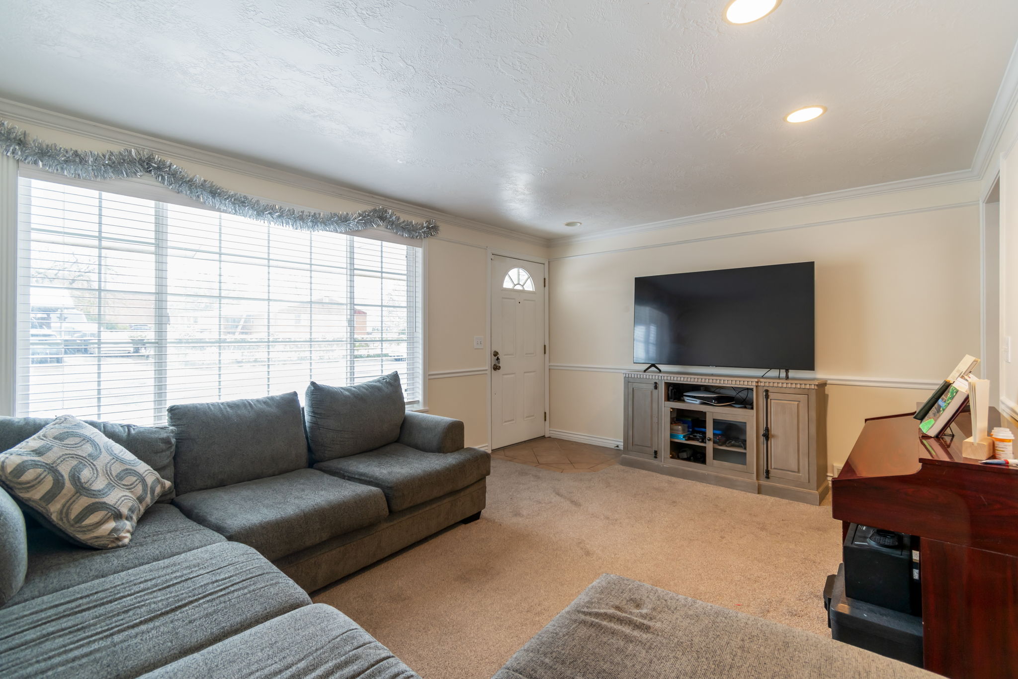Living area featuring a large window with horizontal blinds, recessed lighting, and crown molding