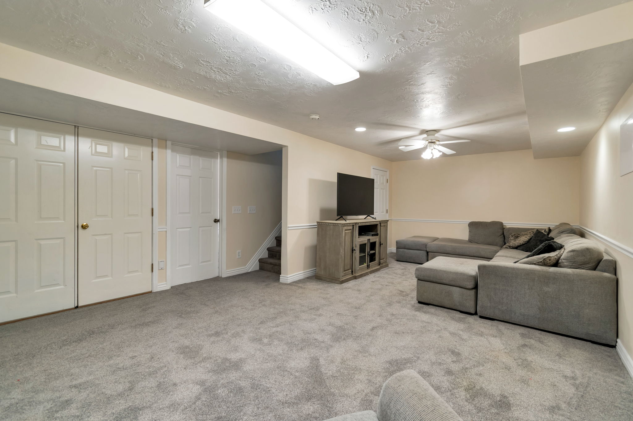 Carpeted room featuring built-in lighting, a ceiling fan, baseboard molding, and multiple paneled doors