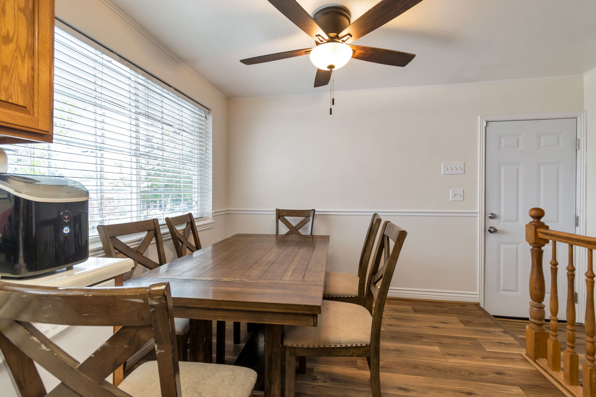 Dining area featuring wood-finish flooring, a contemporary ceiling fan with integrated lighting, a large window with blinds, and wainscoting on the lower wall
