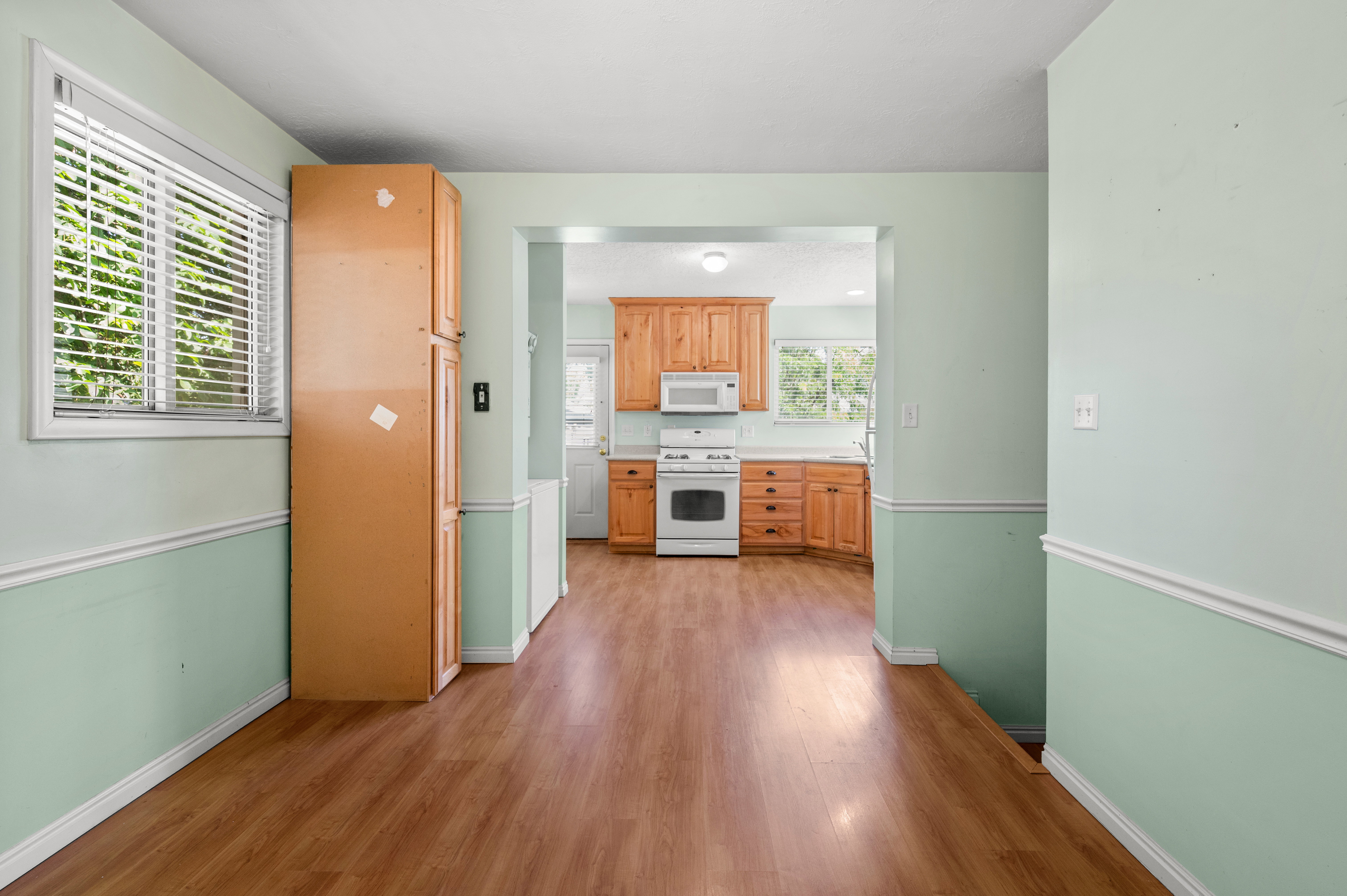 Wood-finish flooring extending from the foreground to the kitchen, featuring light green walls with white chair rail molding