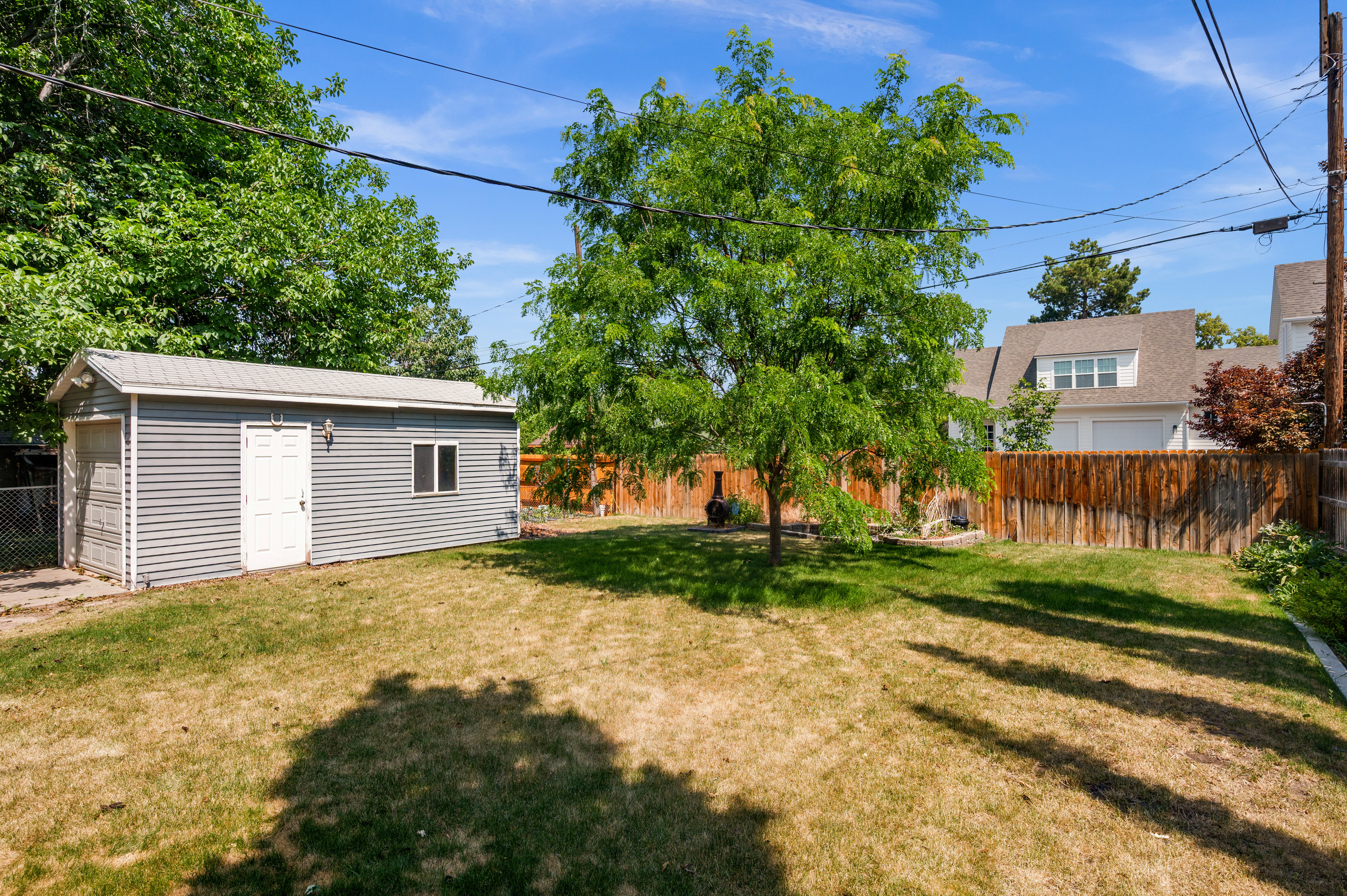 Grassed backyard space featuring a mature tree, a privacy fence, and a detached outbuilding with corrugated siding and a metal roof