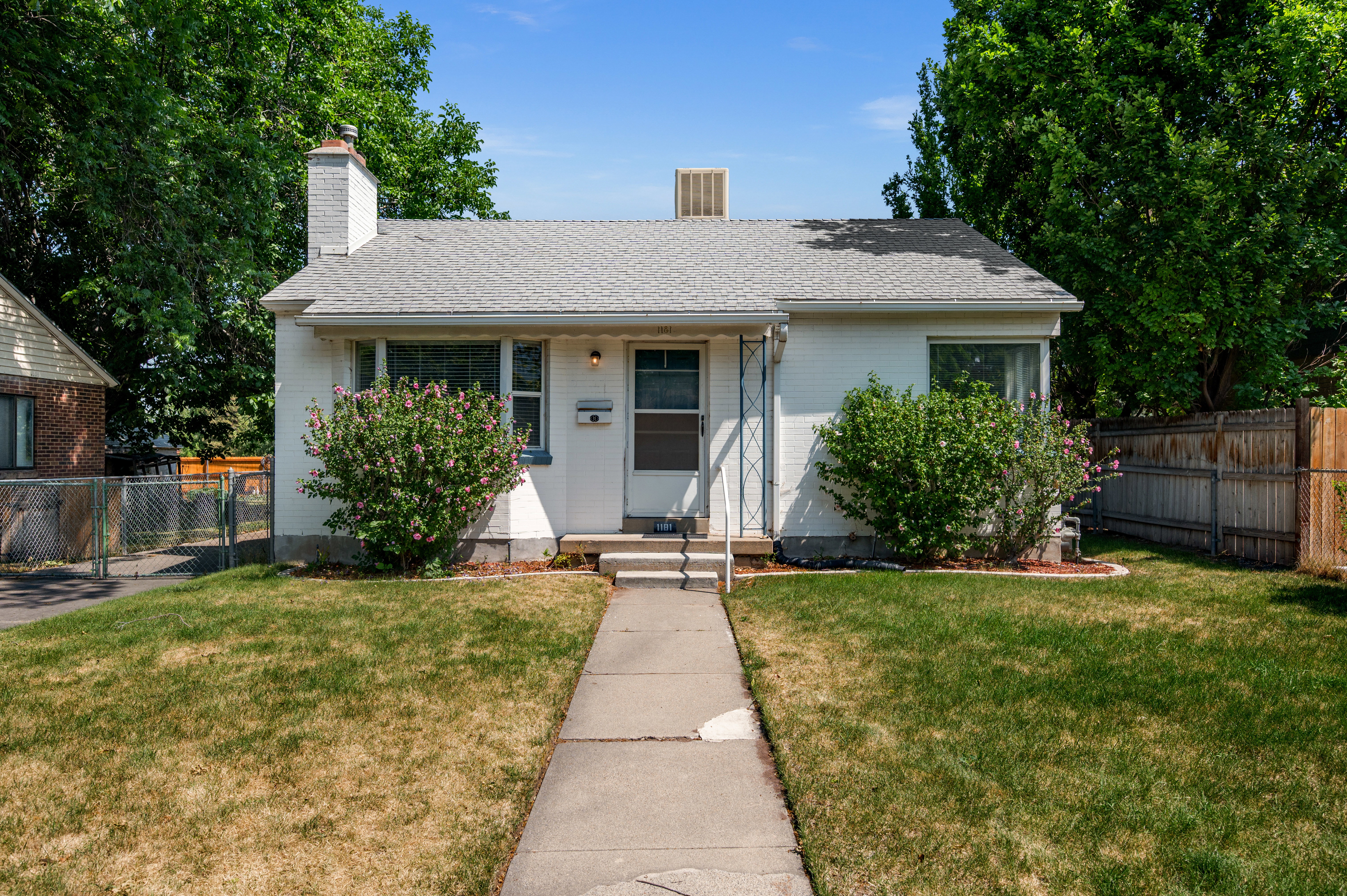 White exterior residence featuring a front lawn, sidewalk, and mature landscaping