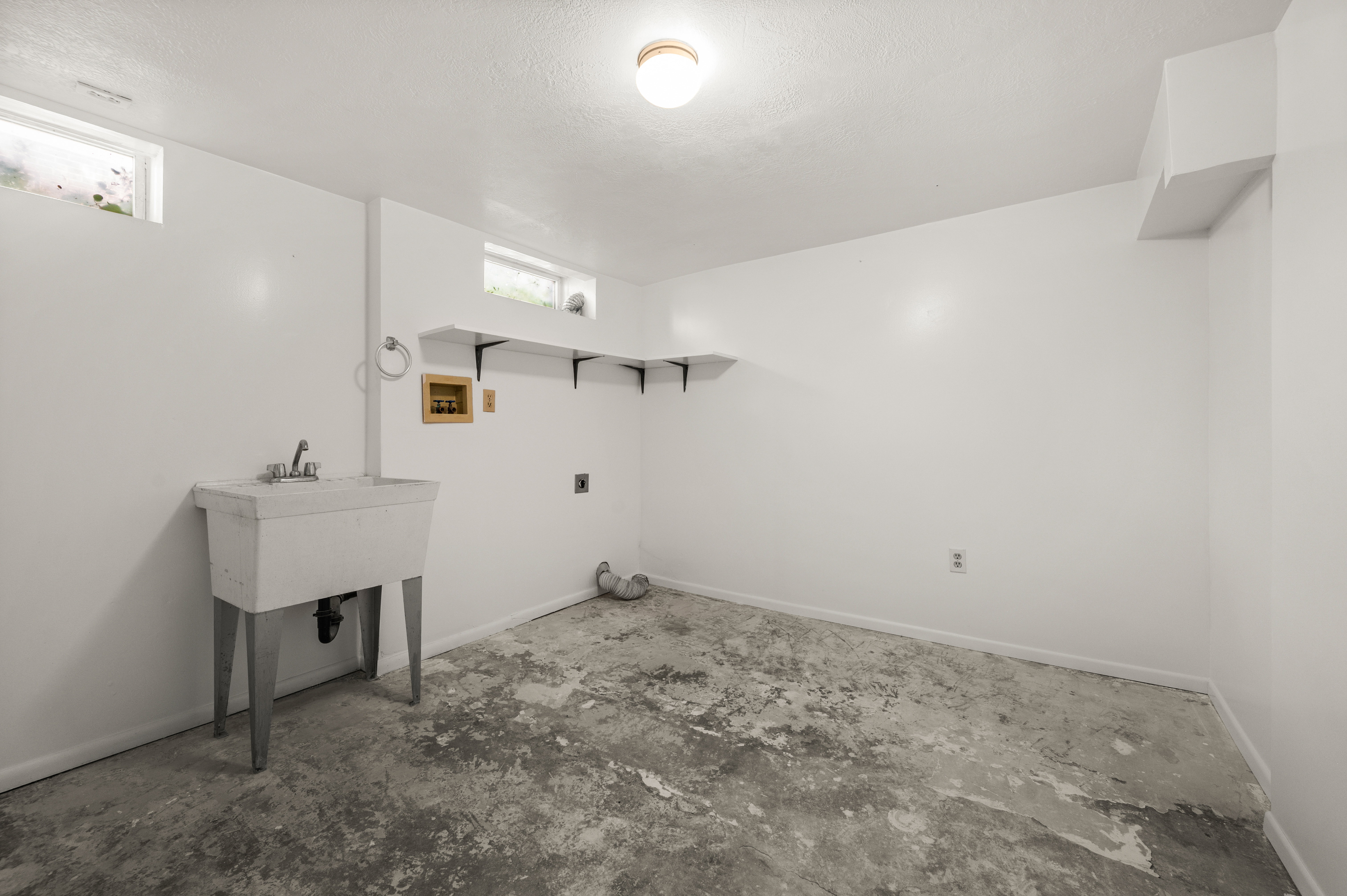 Utility room featuring a built-in wash sink with dual faucets, overhead lighting, and two small windows