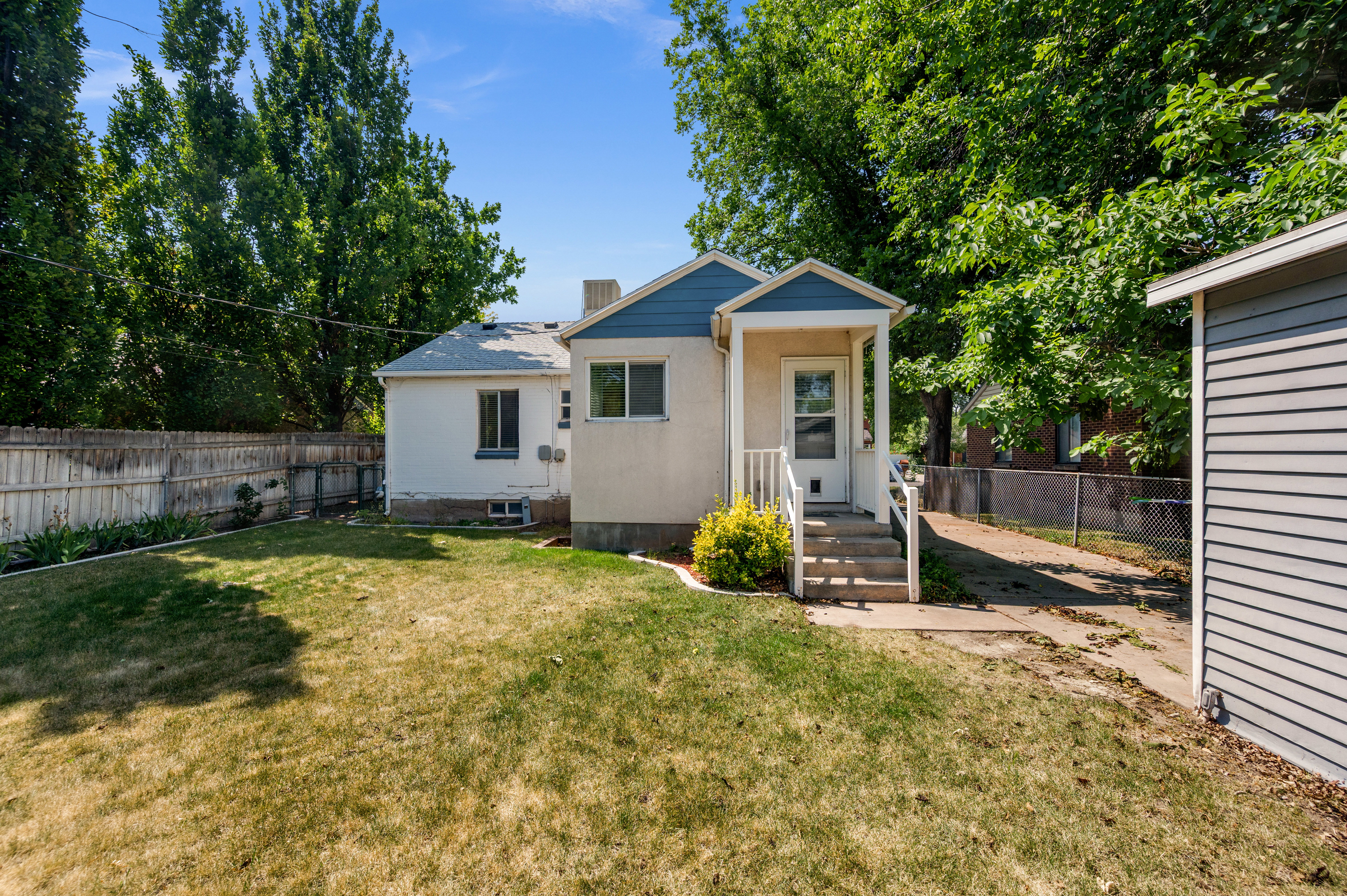 Rear exterior featuring a covered porch entry with white railings, a concrete stairway, and a small landscaped area