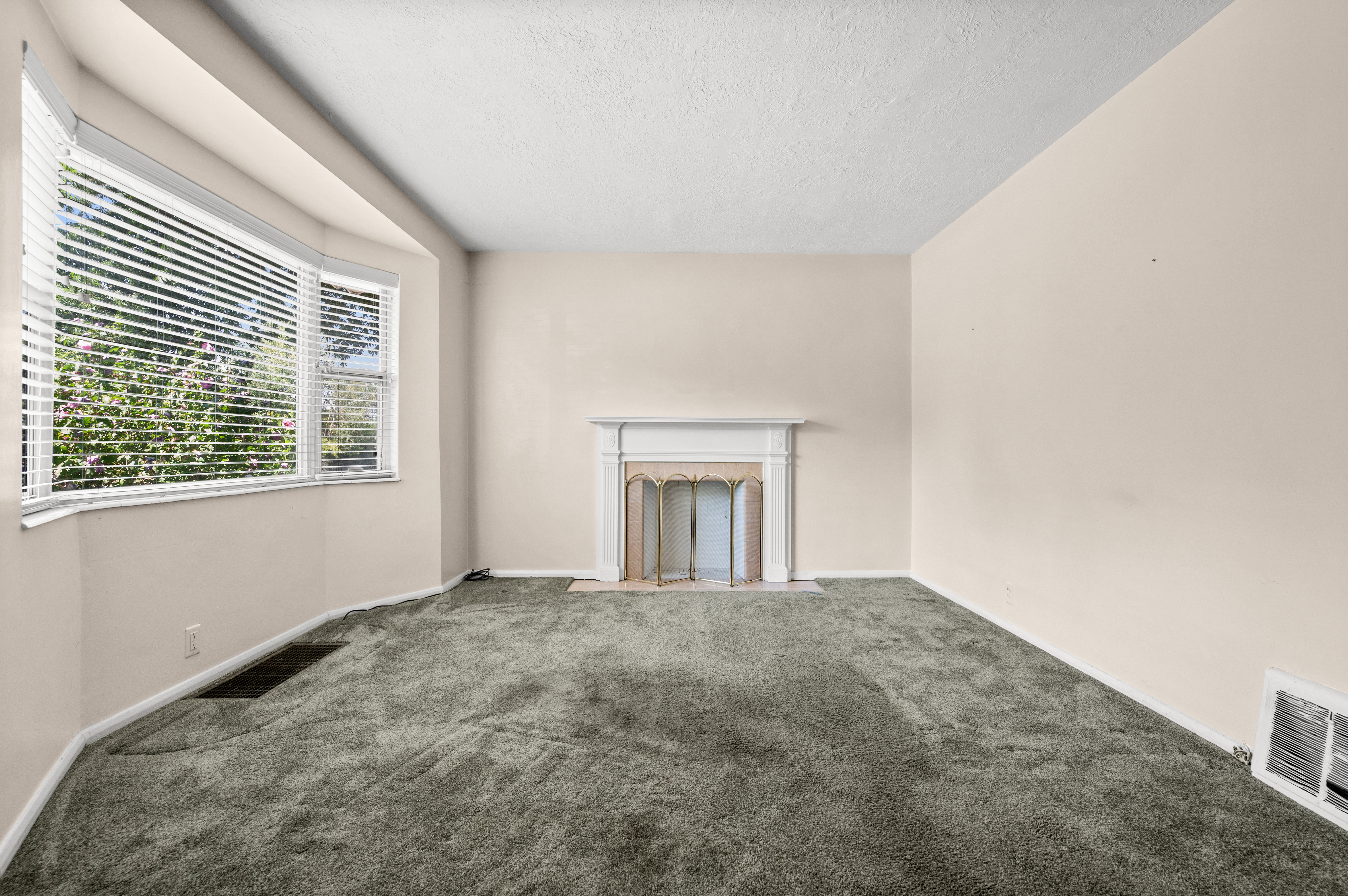 Room featuring a bay window with blinds, a white fireplace surround, and light-colored walls