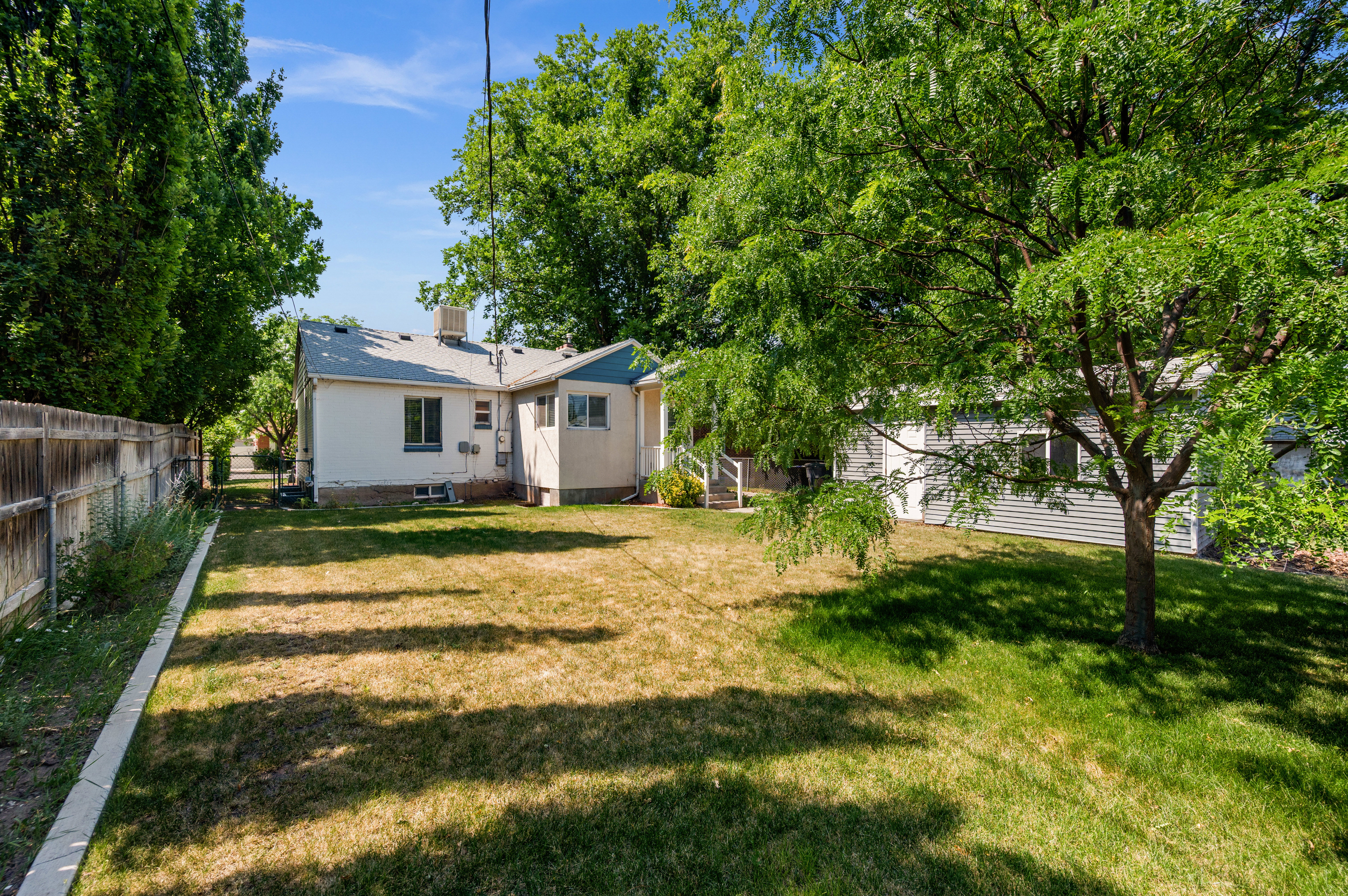 Expansive backyard featuring a fenced perimeter, mature shade trees, and a detached structure with siding