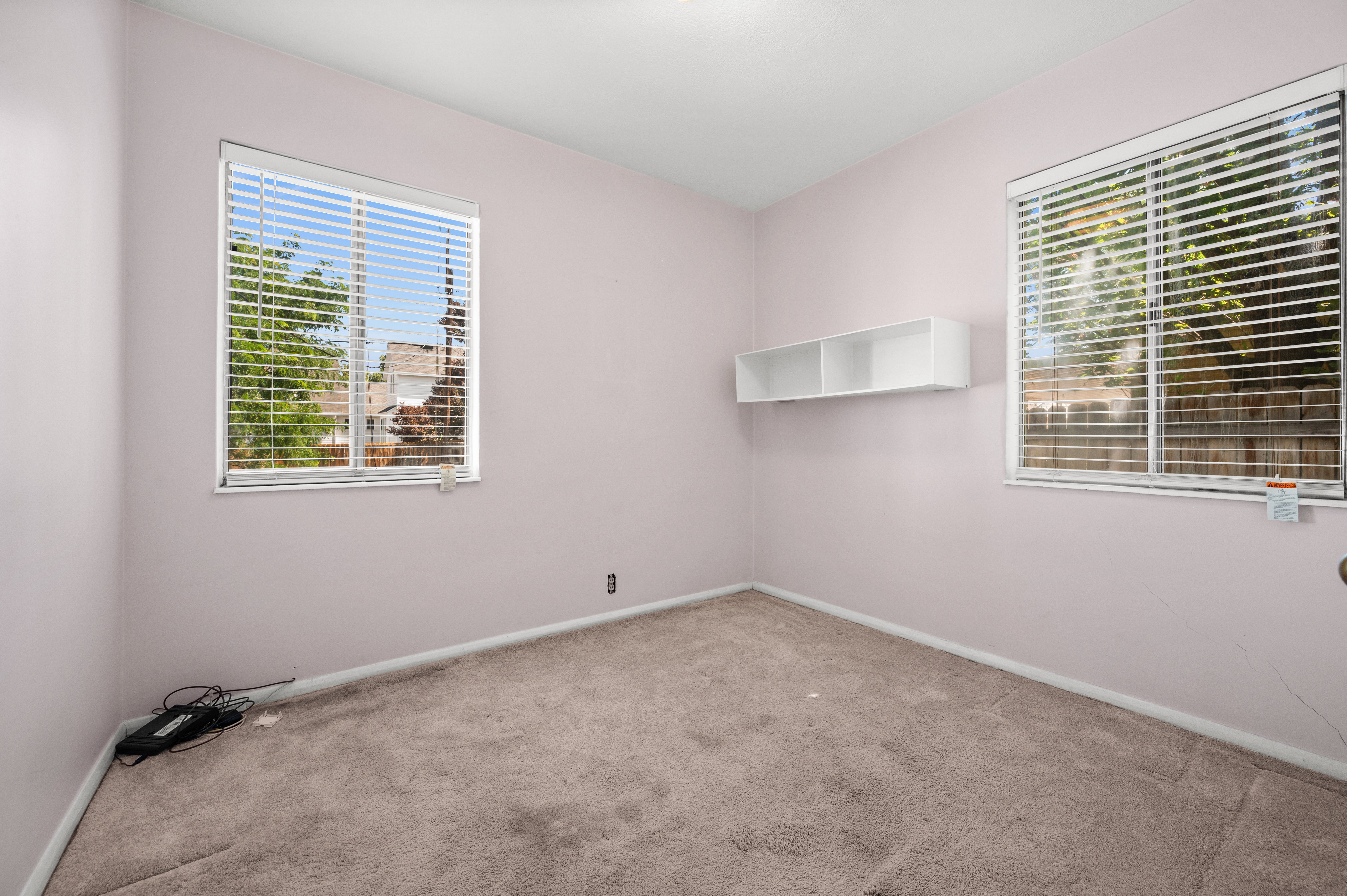 Carpeted room with two windows featuring blinds, a built-in wall shelf, and a ceiling light fixture