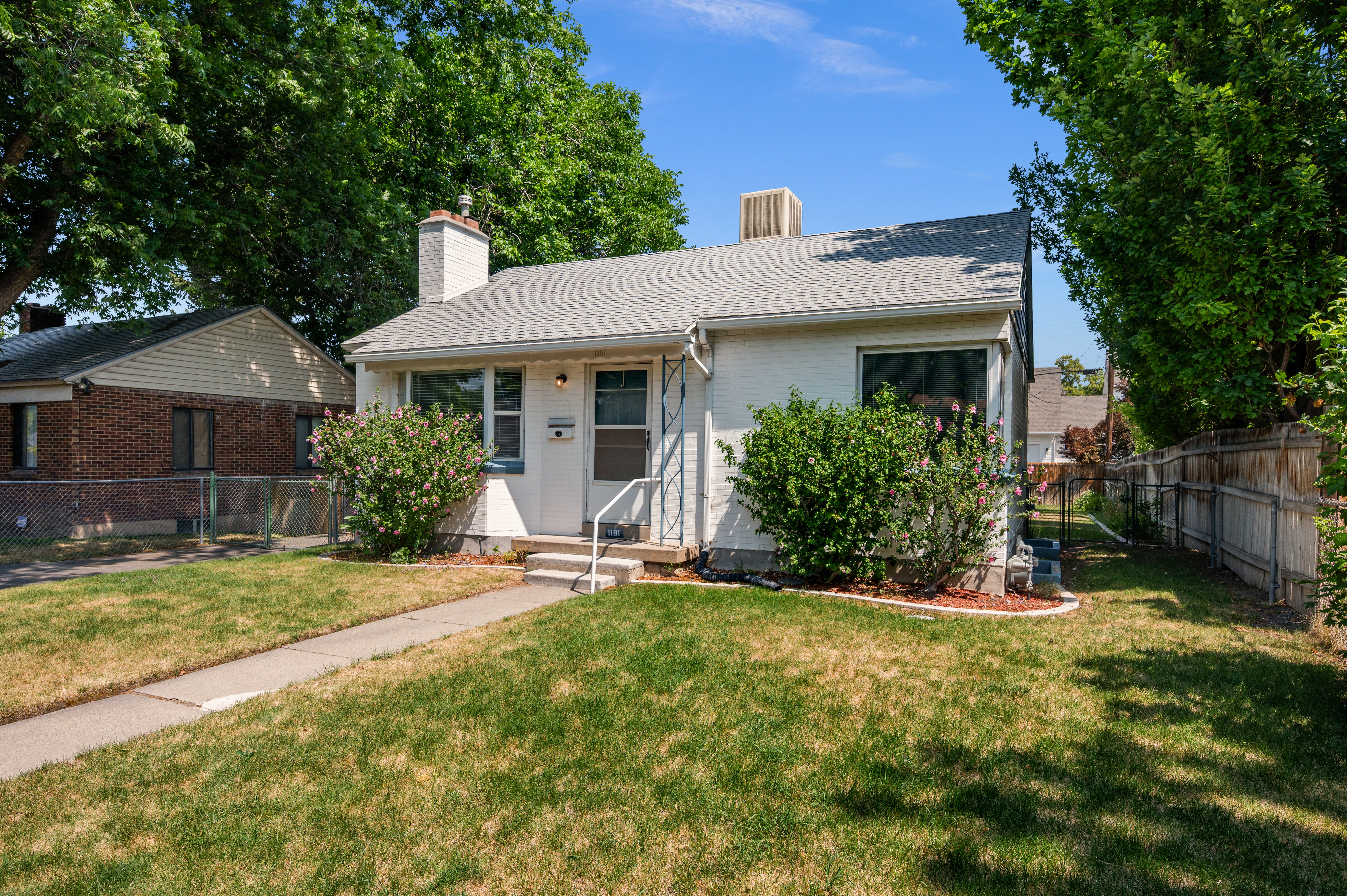 White stucco exterior with a gray shingled roof and prominent brick chimney
