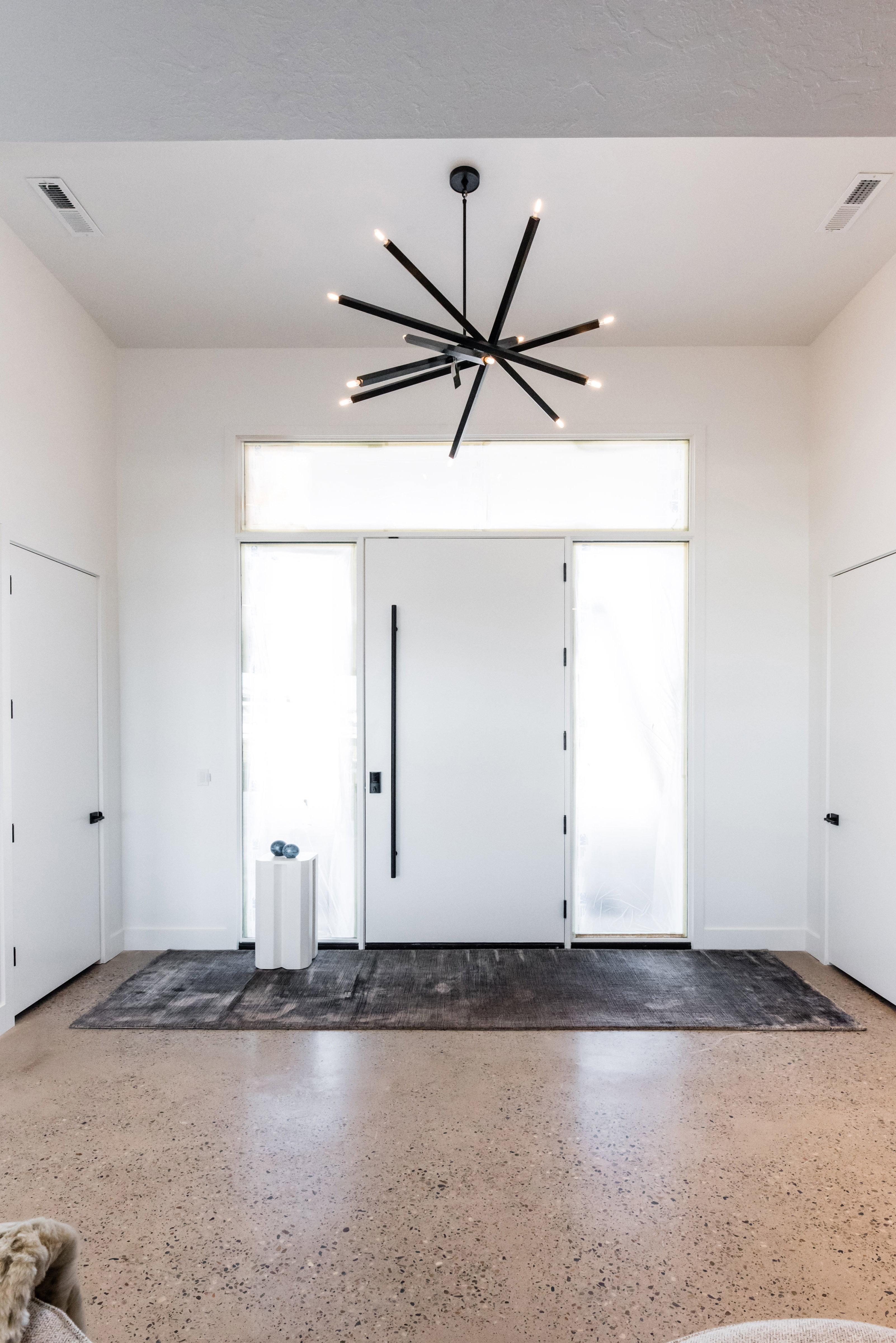 Entryway featuring a black modern sputnik chandelier, a white solid core entry door with a vertical pull handle, frosted sidelight windows, and polished concrete flooring