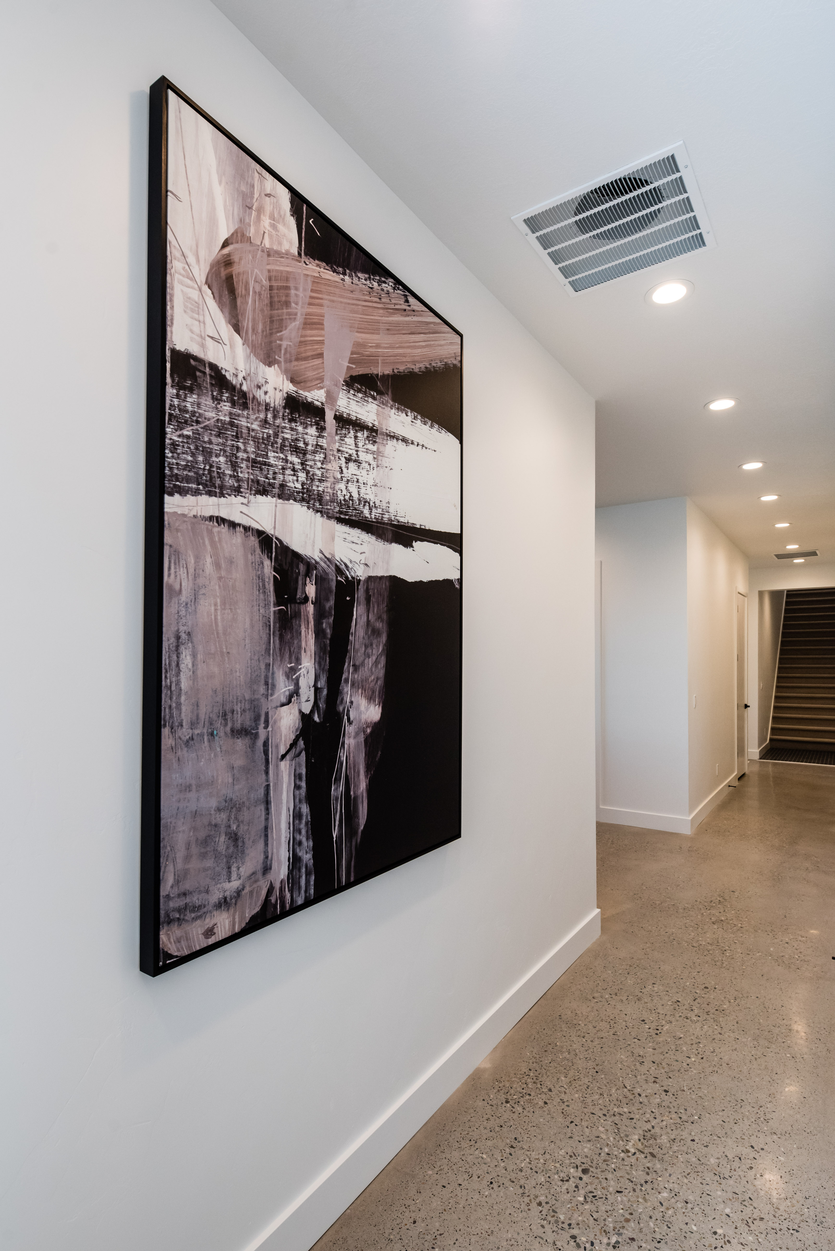Polished concrete flooring, recessed lighting, and a white baseboard trim create a streamlined hallway aesthetic