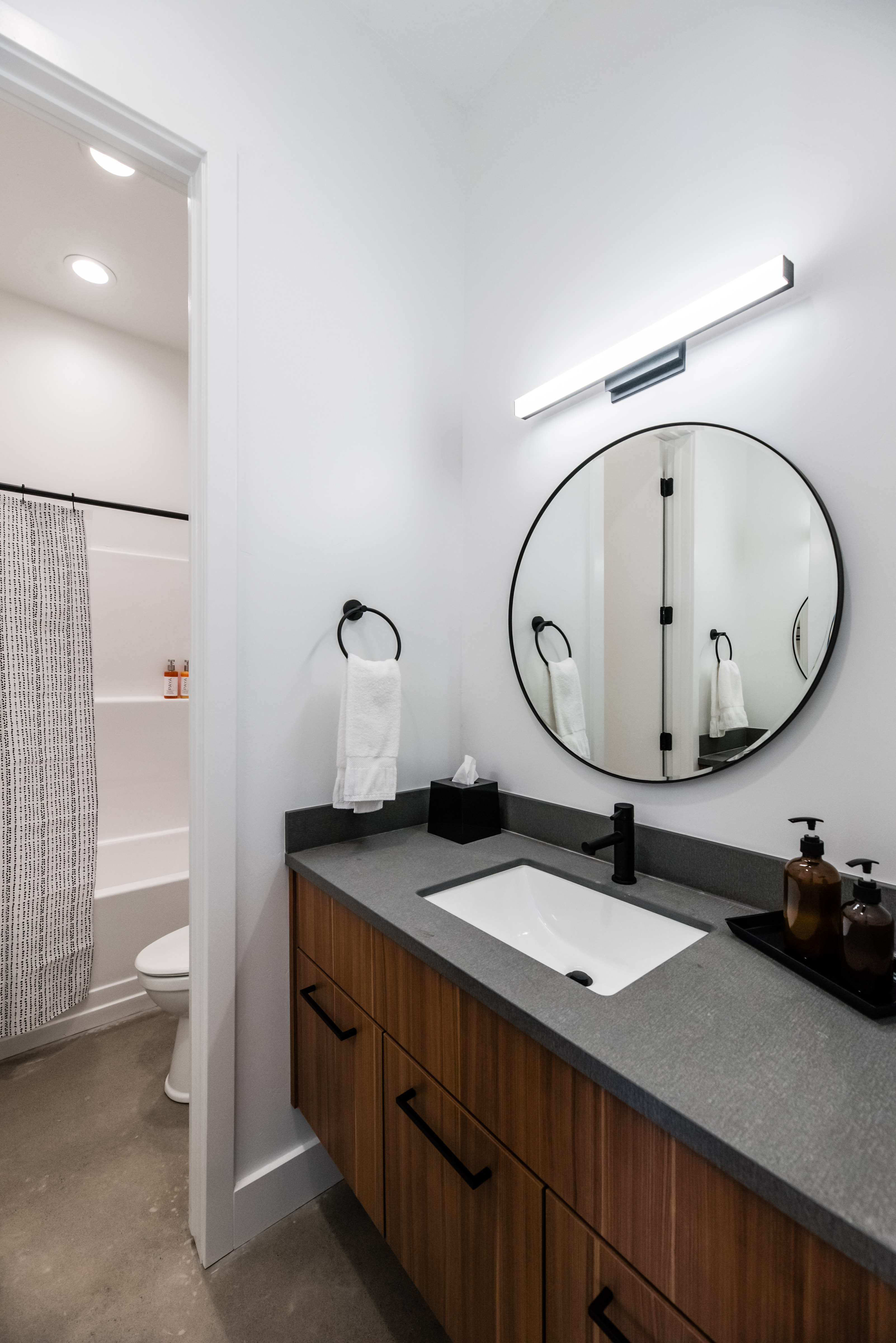 Floating wood-finish vanity with a rectangular undermount sink, dark countertop, and matte black faucet