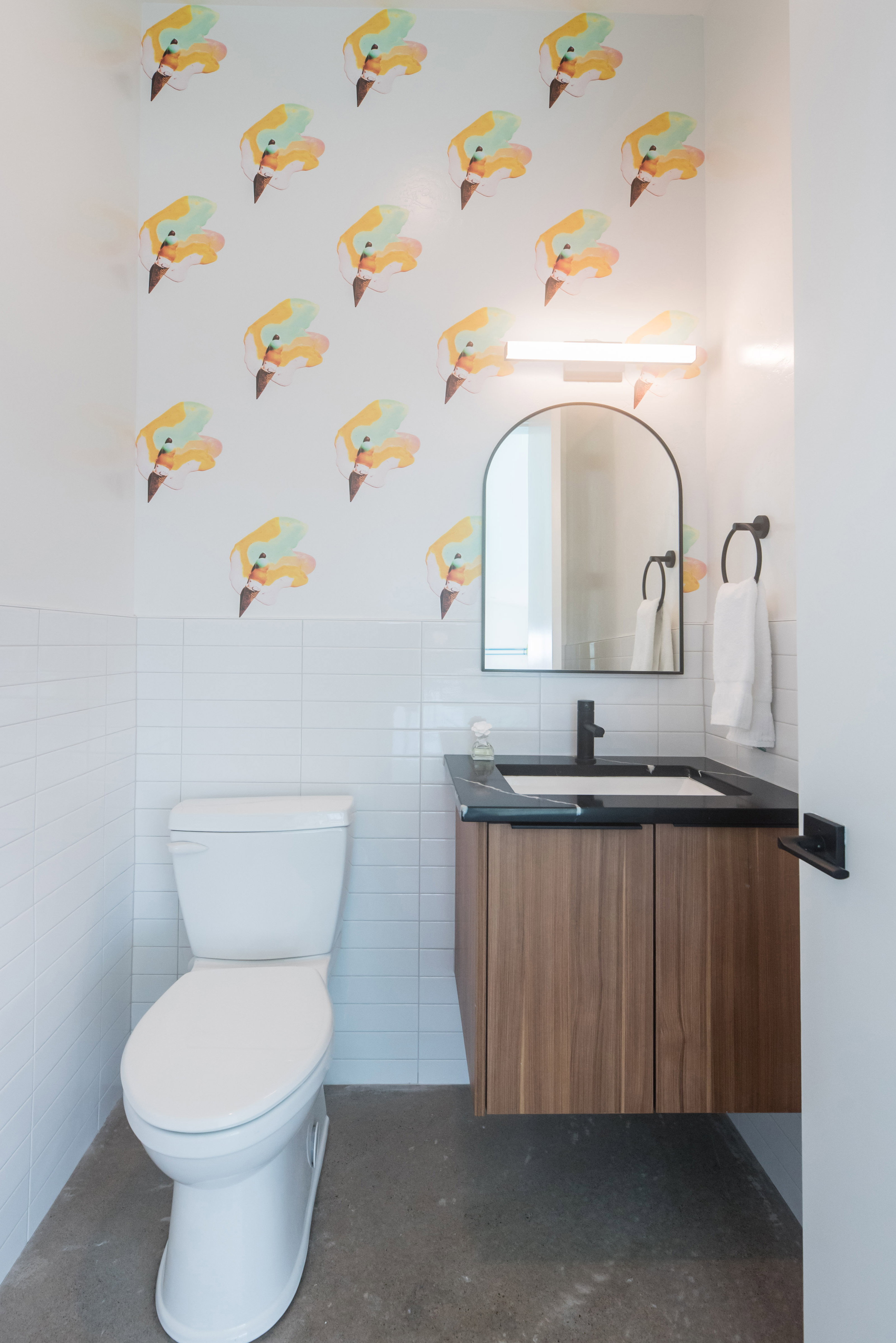 Modern powder room featuring a floating wood-finish vanity with a dark countertop and integrated sink, white subway tile wainscoting, and a decorative accent wall