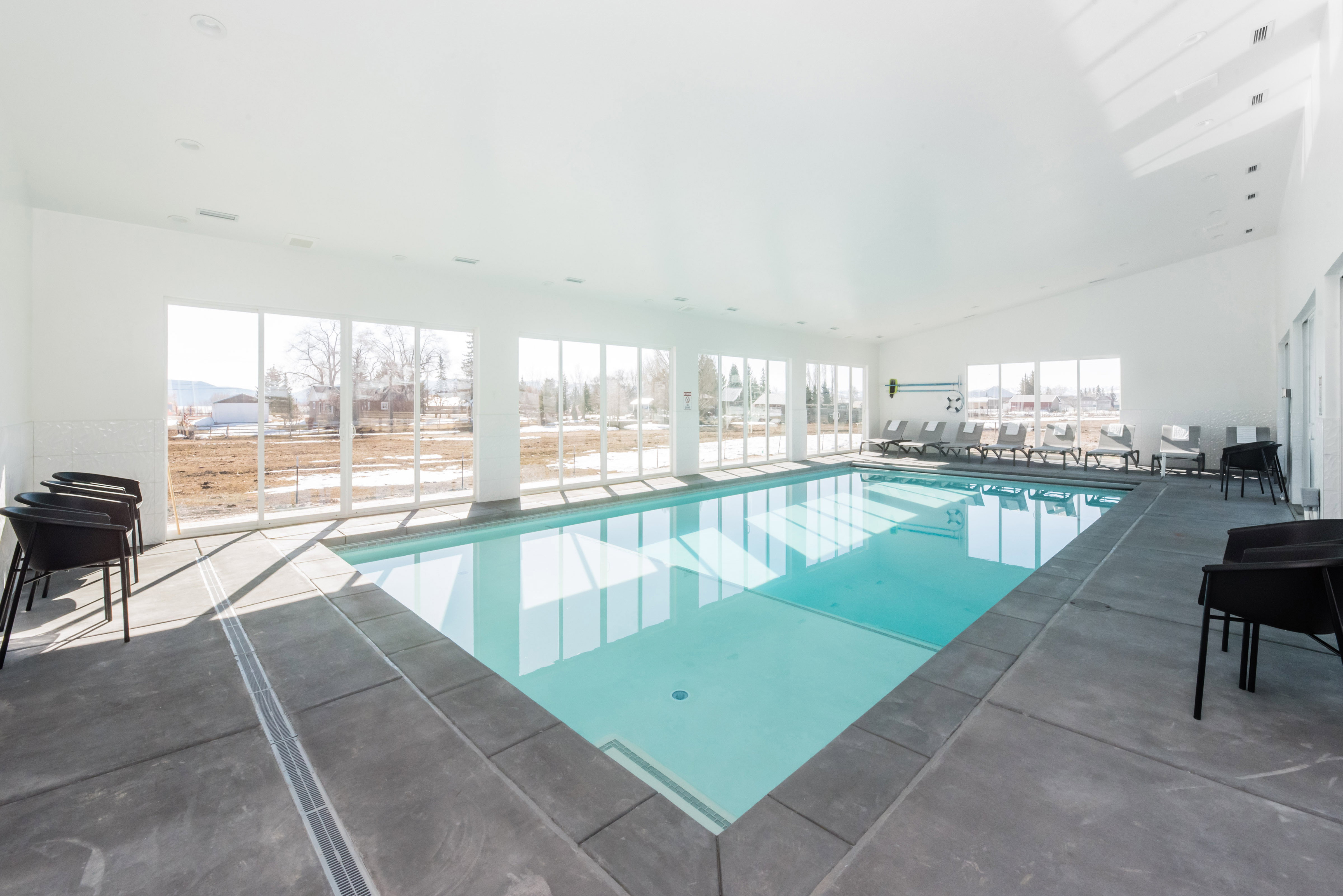 Indoor swimming pool featuring a bright white interior, extensive window walls, recessed lighting, and a durable perimeter deck