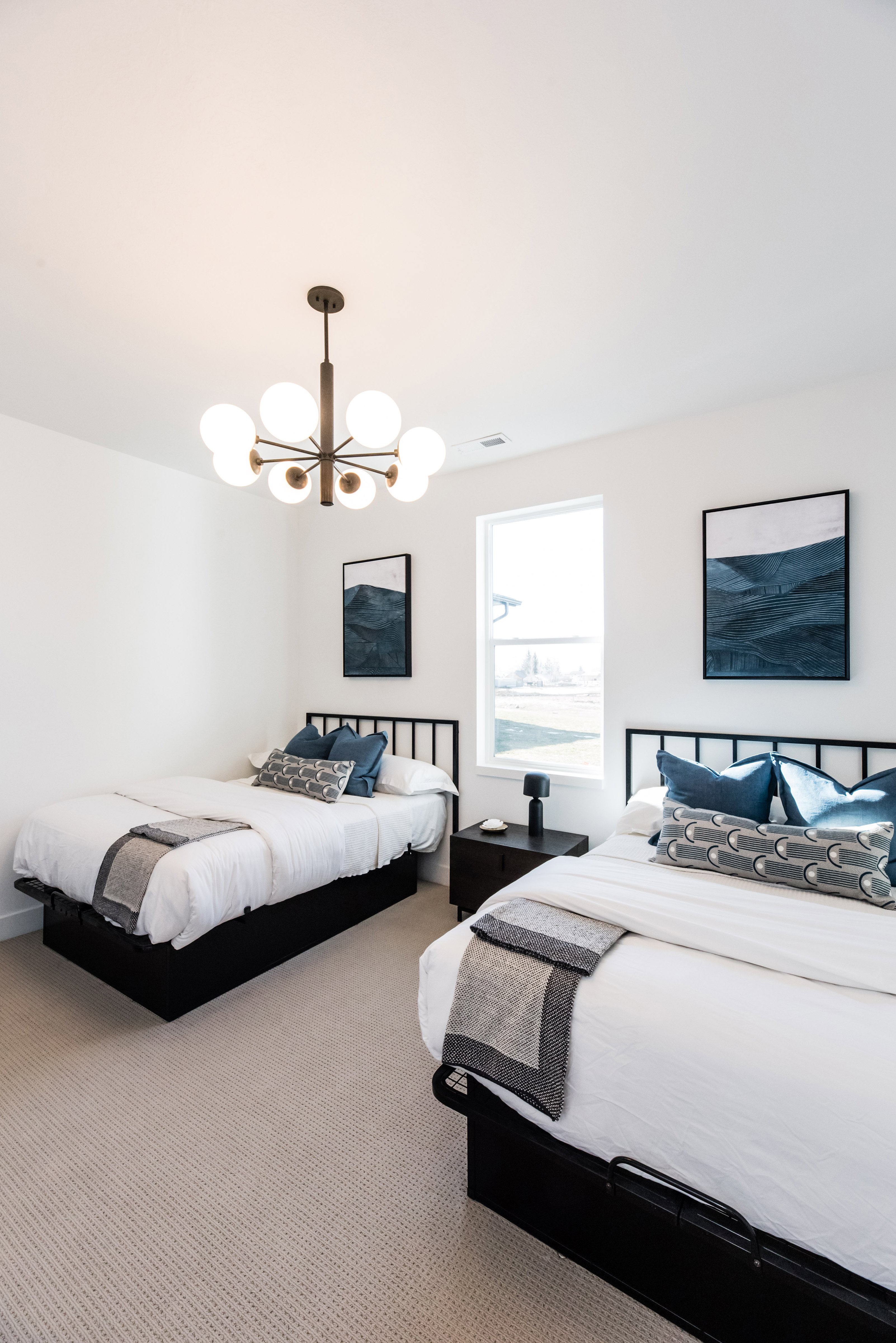 Bright room featuring a modern multi-bulb chandelier, soft textured carpeting, and a large window providing ample natural light