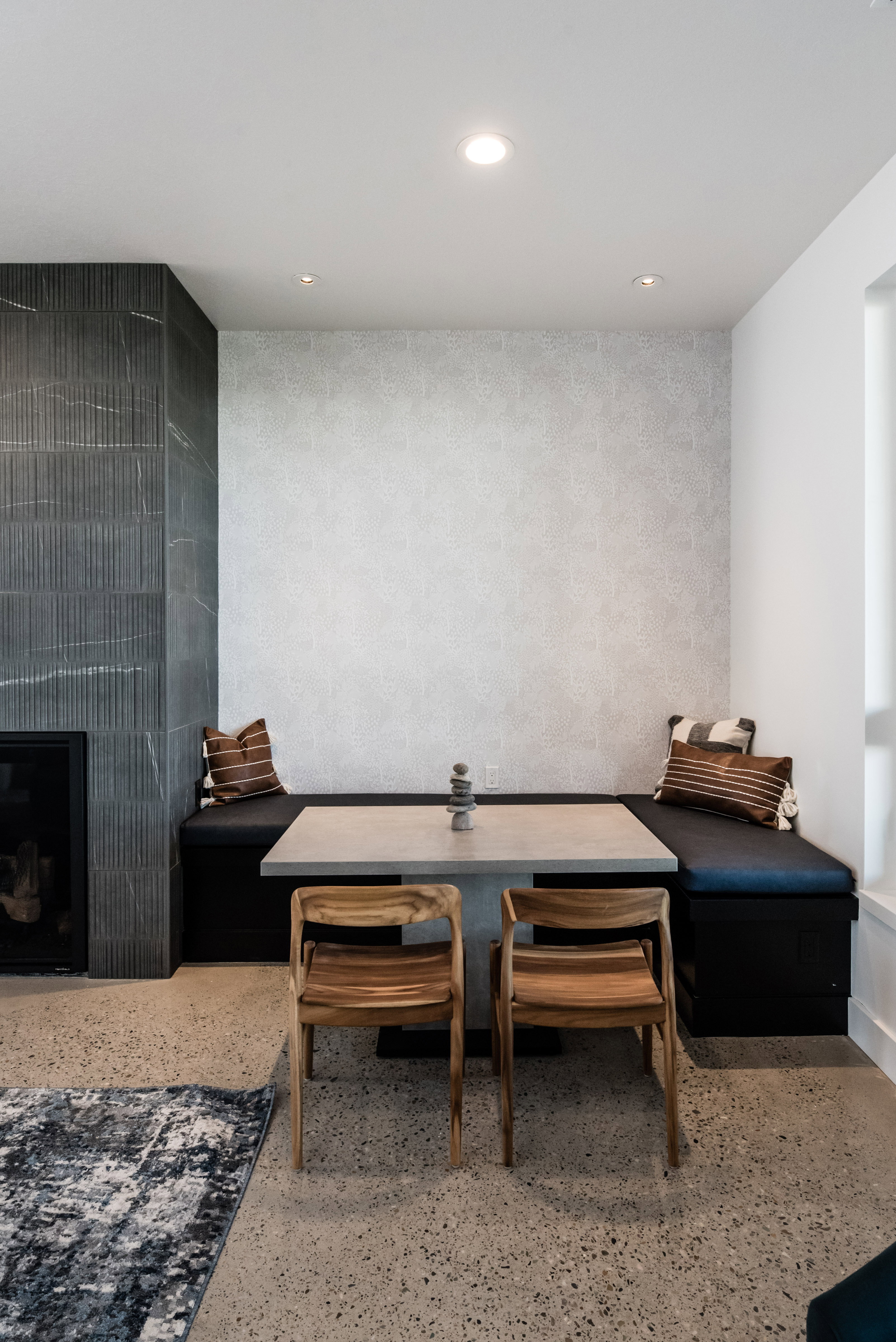 Built-in banquette seating with a square table, adjacent to a fireplace with textured tile surround