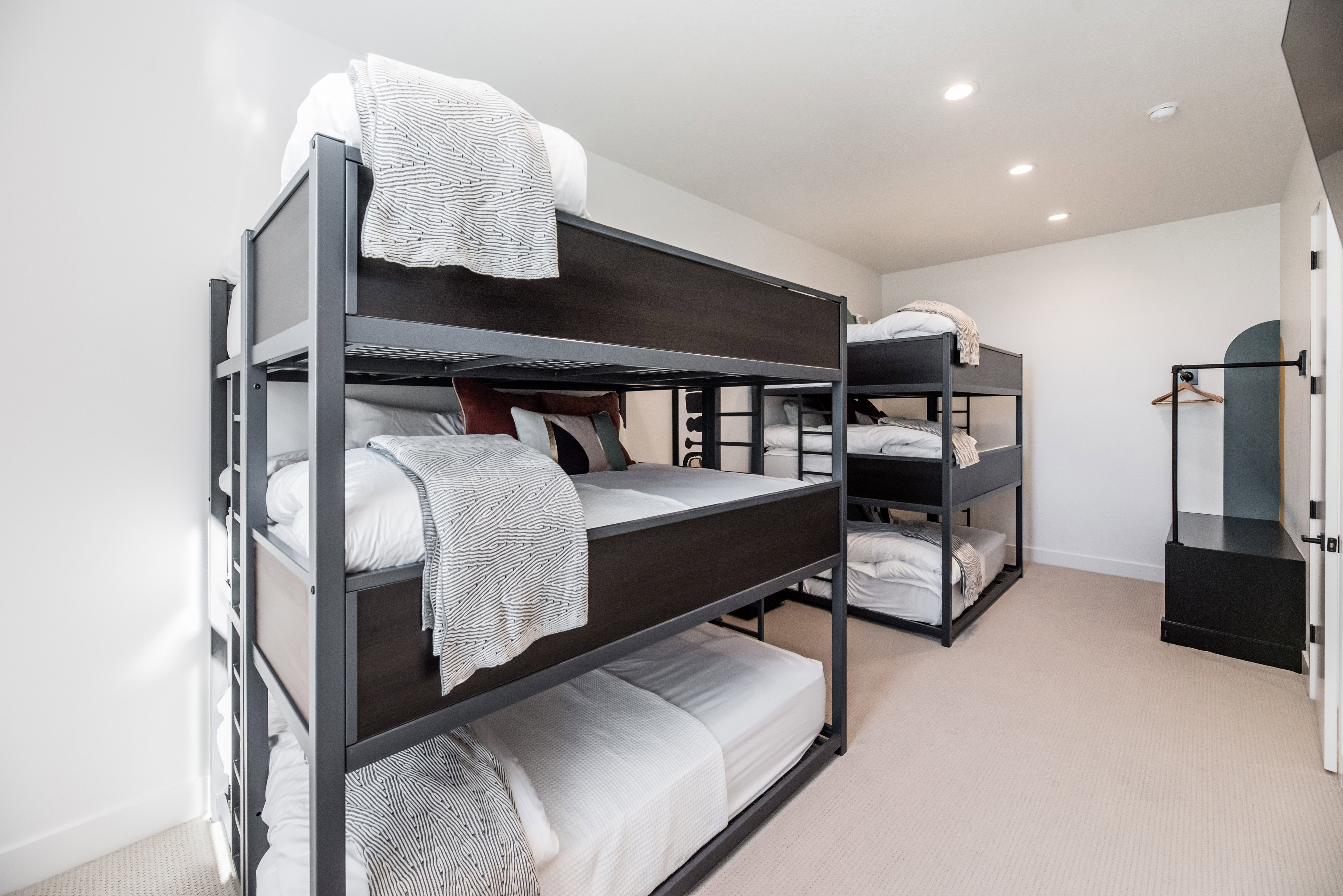 Room featuring multiple bunk beds with dark frames and white bedding, recessed ceiling lighting, light-colored carpet, and a built-in wardrobe with an arched accent