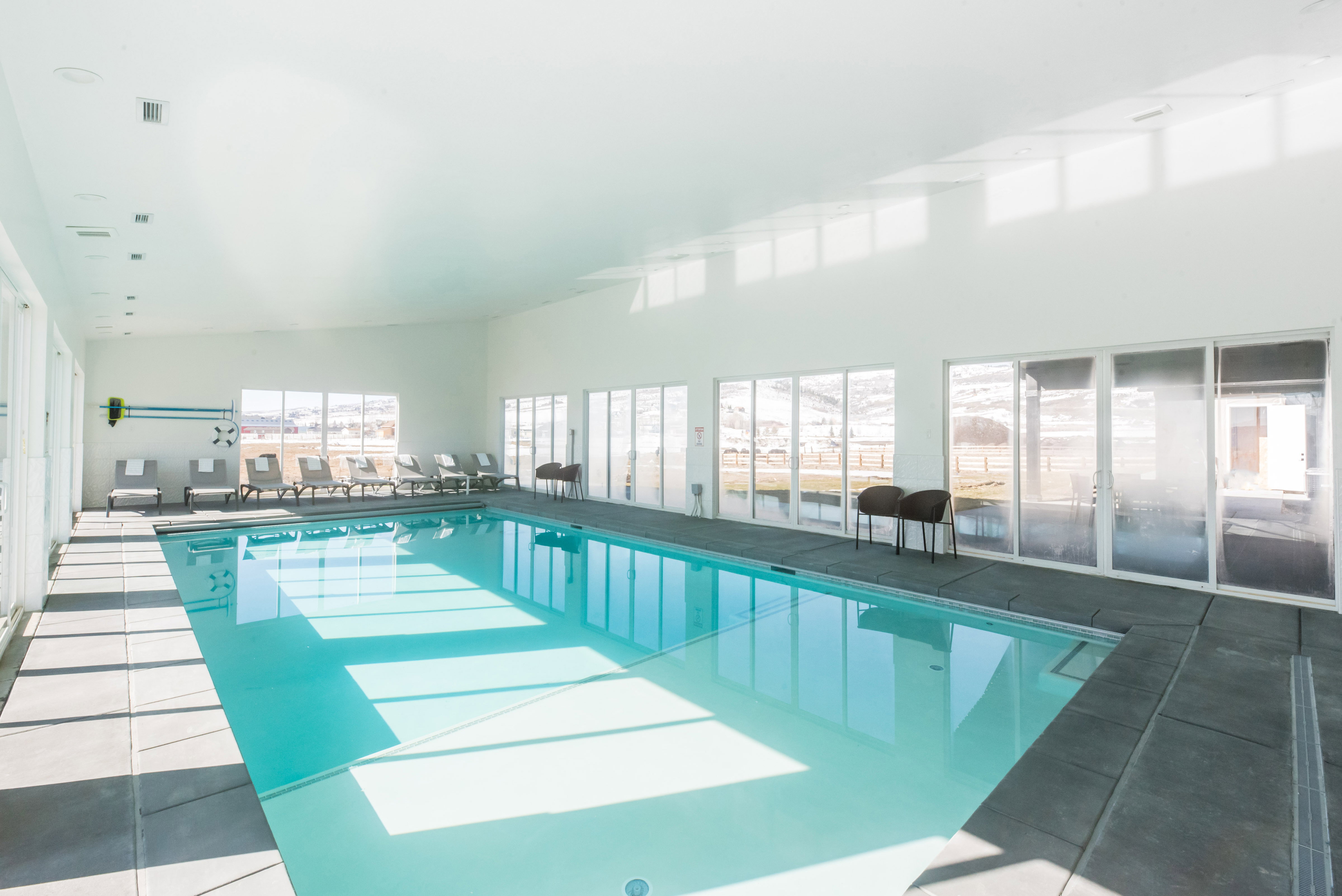 Indoor swimming pool with large format tile surround, expansive windows, recessed lighting, and white walls