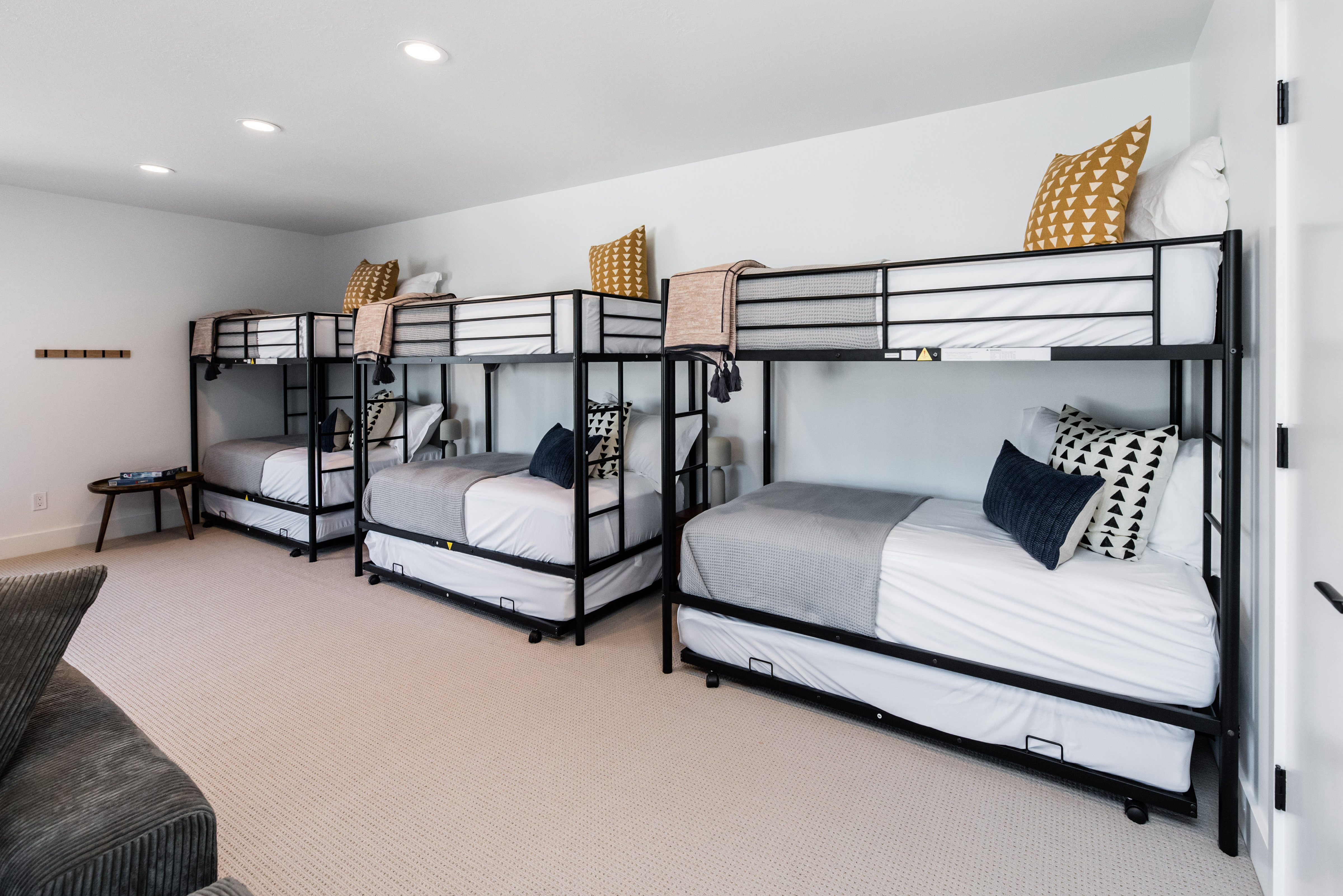 Spacious room featuring multiple metal bunk beds with pull-out trundles, recessed lighting, white baseboards, and light-toned carpeting