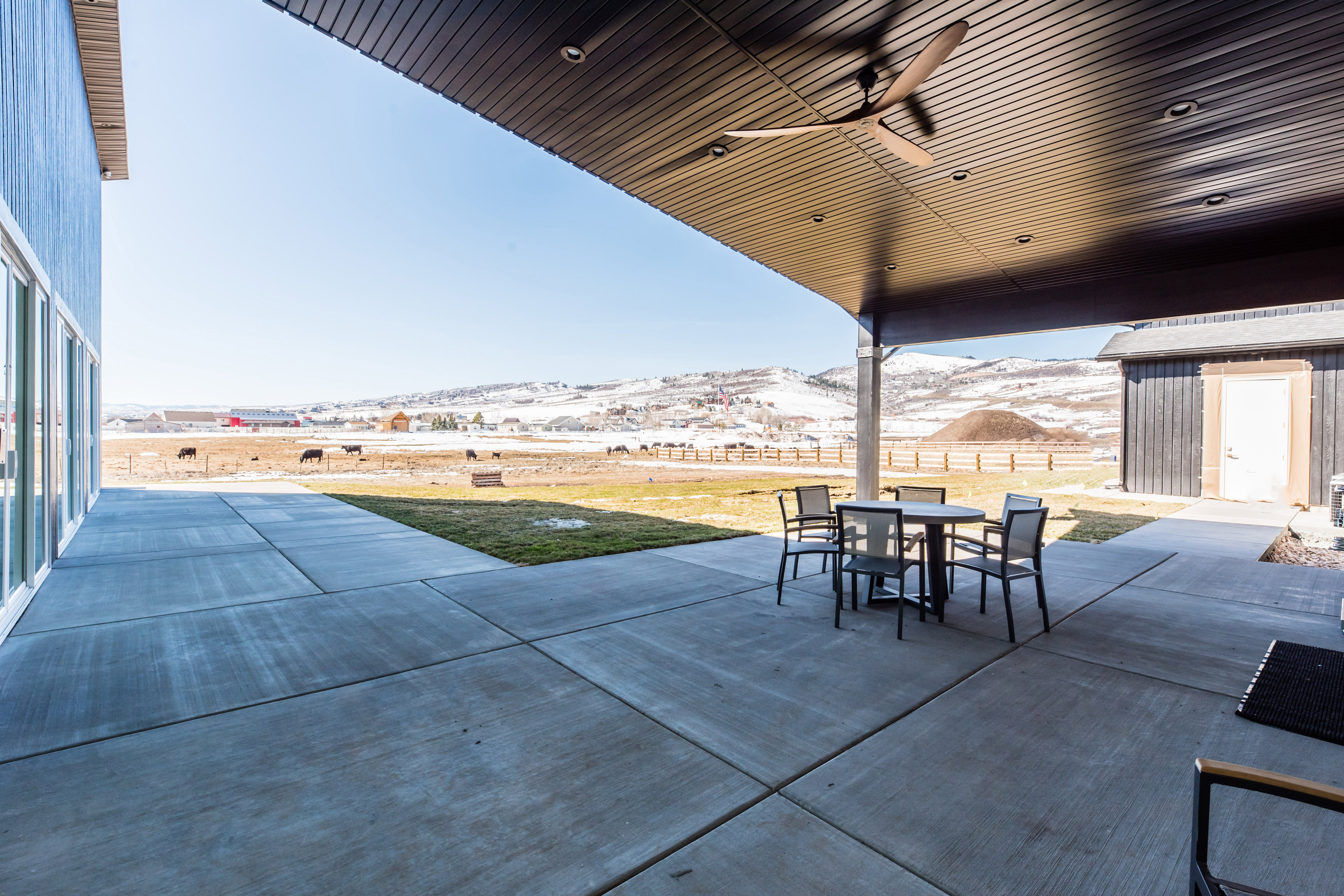 Expansive concrete patio featuring a dark wood-finish ceiling with recessed lighting and a ceiling fan