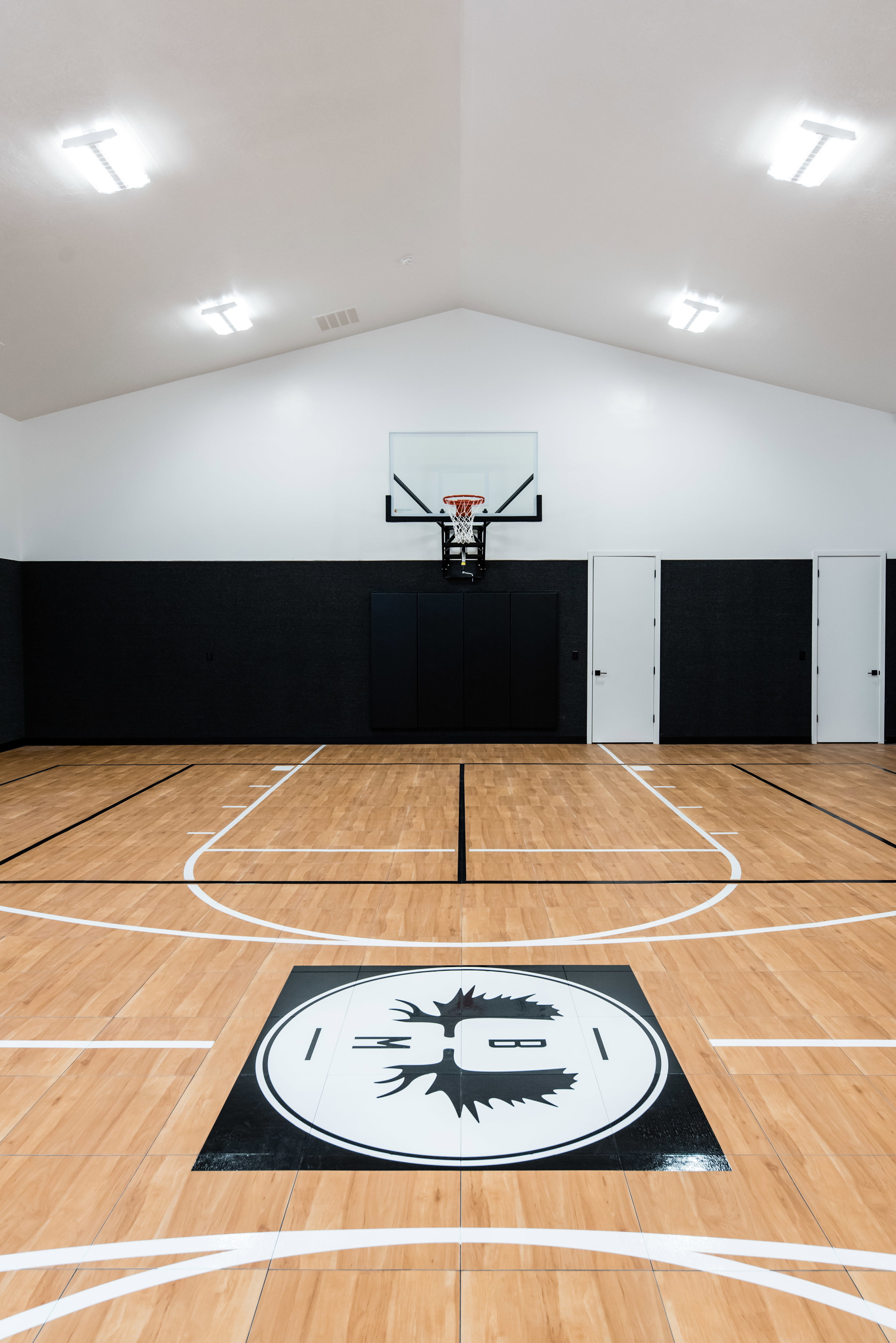 Indoor basketball court featuring wood-finish flooring with court markings, a mounted hoop, and a custom floor logo