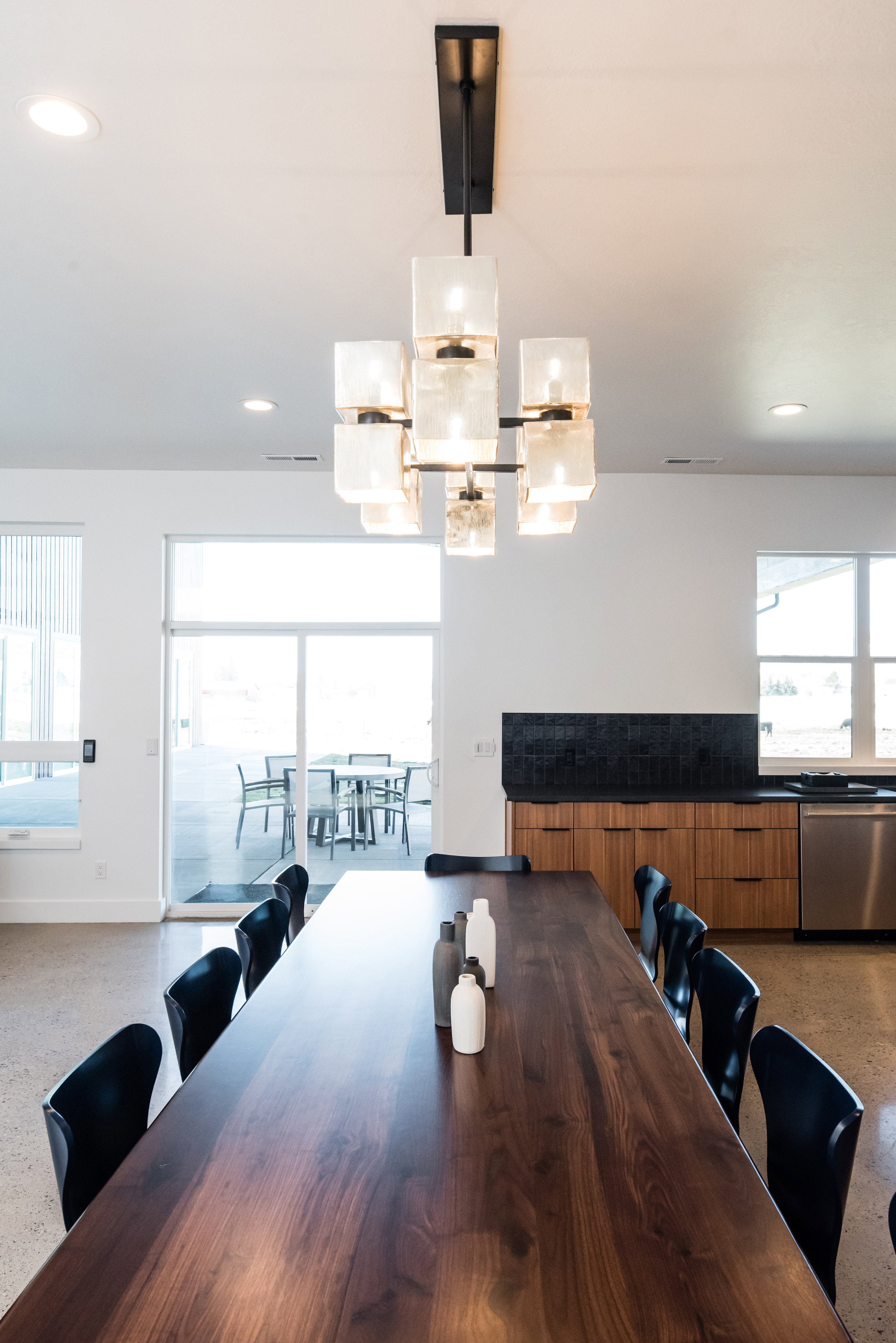 Spacious dining area featuring a dark wood-finish table, a contemporary chandelier, recessed ceiling lighting, and polished concrete flooring