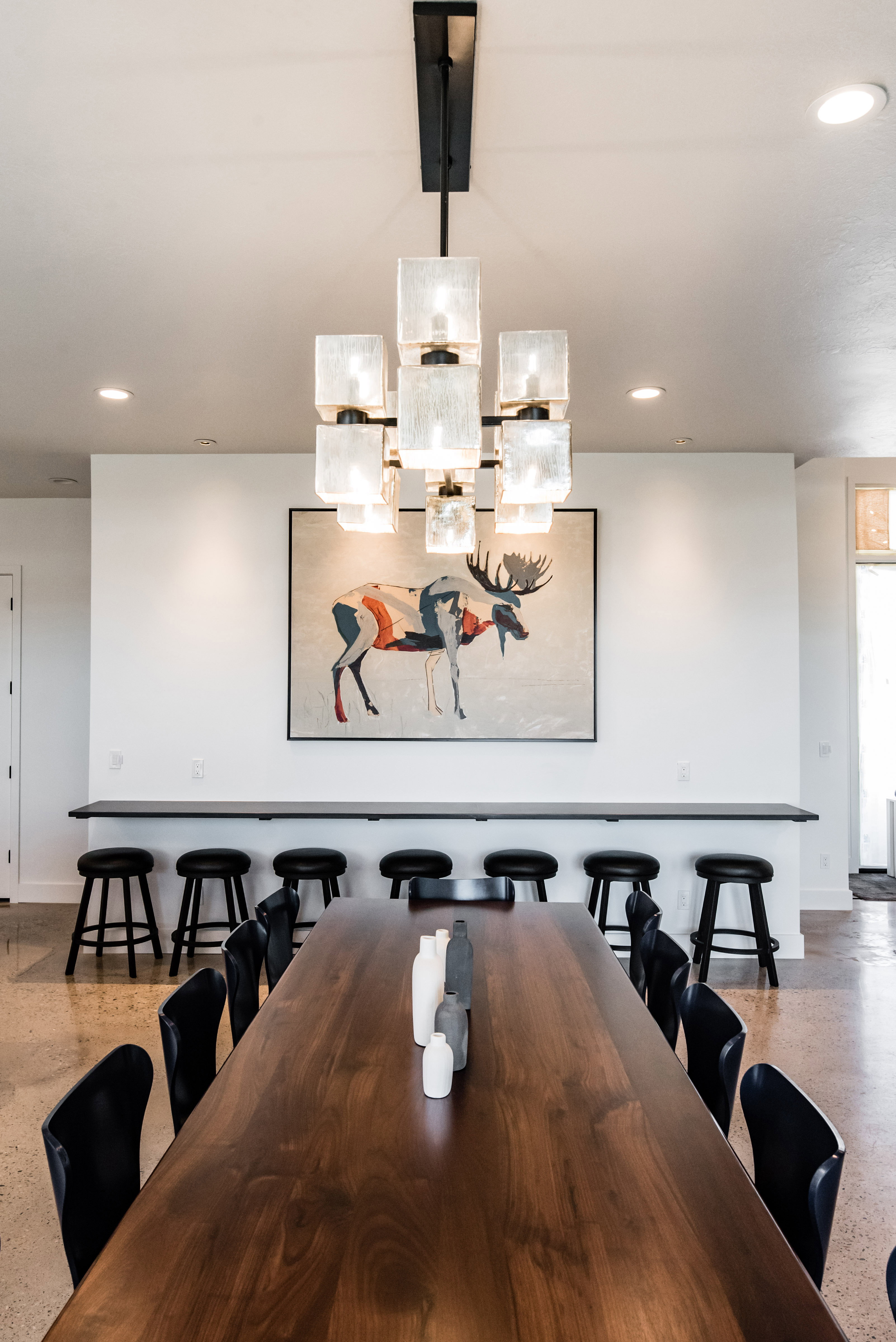 Spacious dining area featuring a tiered contemporary chandelier, wood-finish flooring, and a long wood-finish dining table