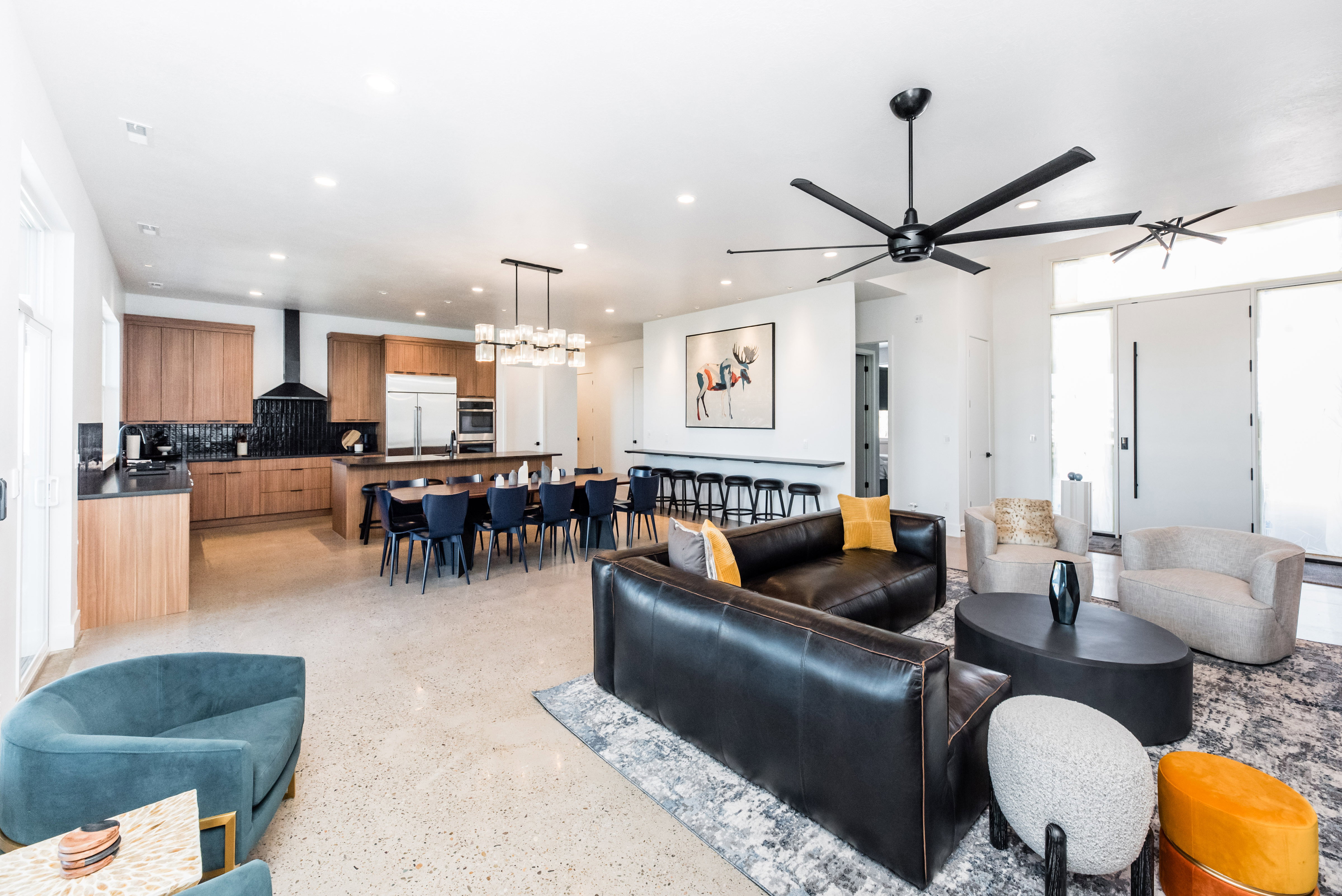 Open-concept living area featuring light-toned flooring, a kitchen with wood-finish cabinetry, a large dining island, and a contemporary black ceiling fan