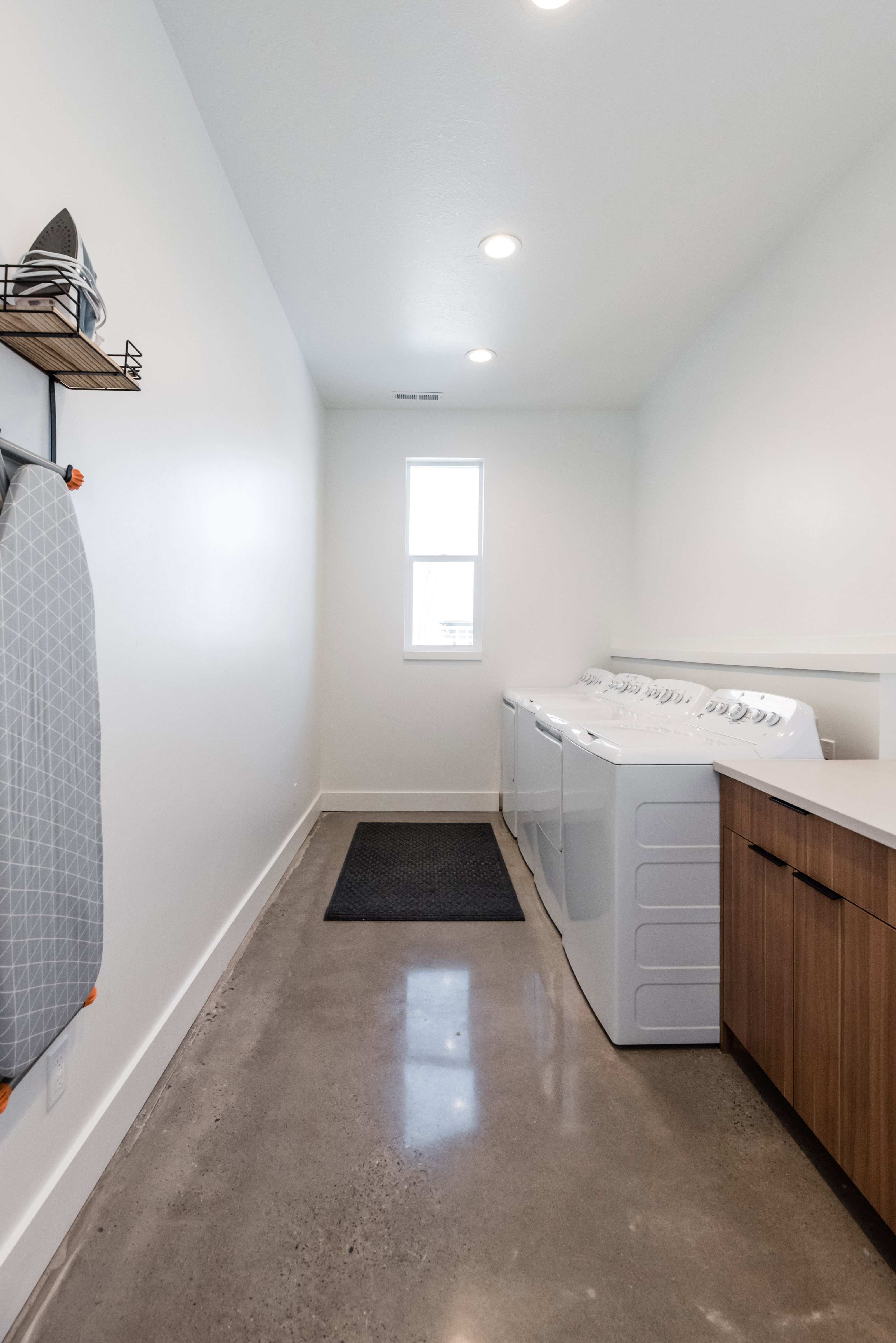 Utility room featuring concrete flooring, a single window, recessed lighting, and a built-in counter with wood-finish cabinetry
