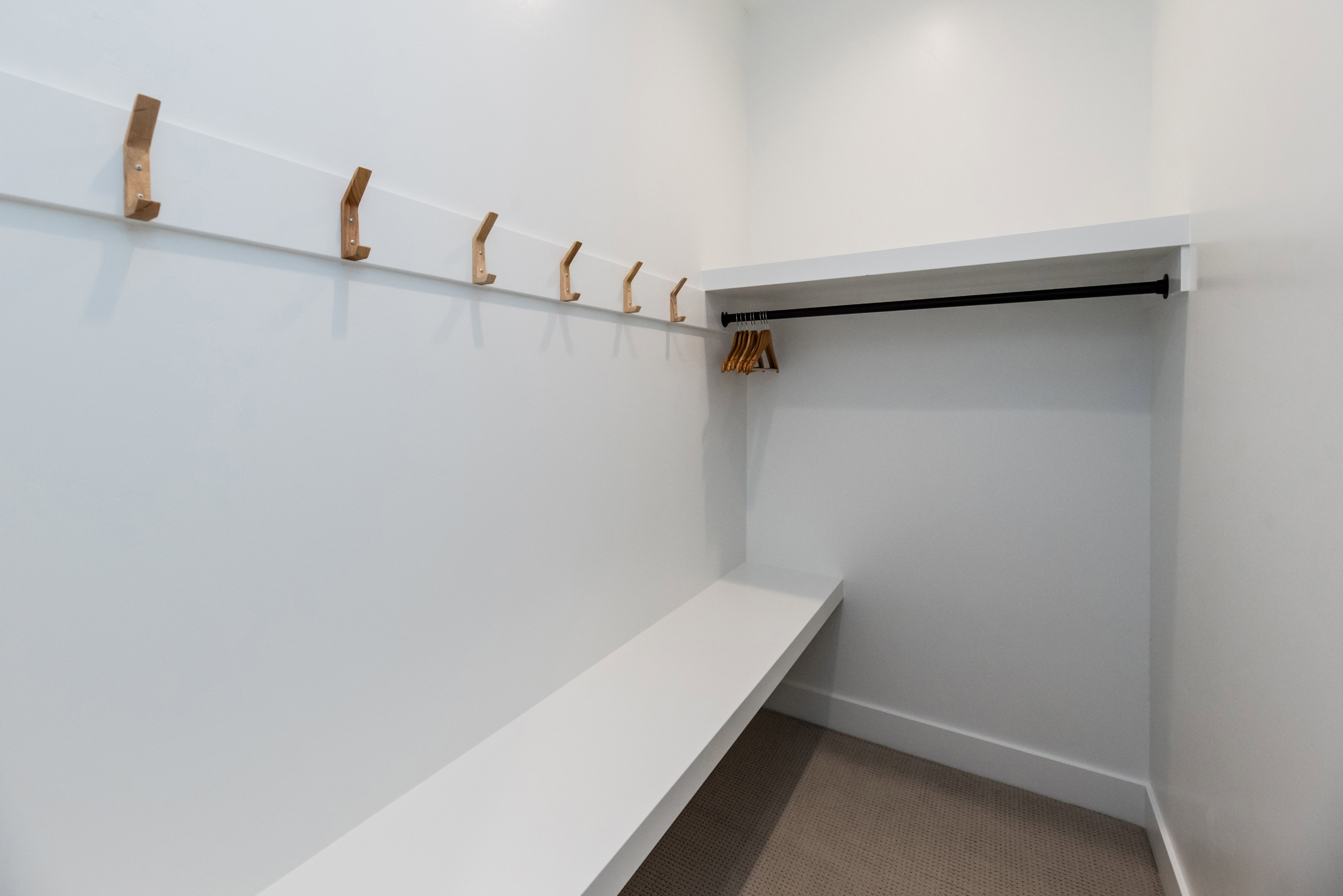 Entryway mudroom featuring a built-in bench, seven wall-mounted hooks, overhead shelving, and a garment rod