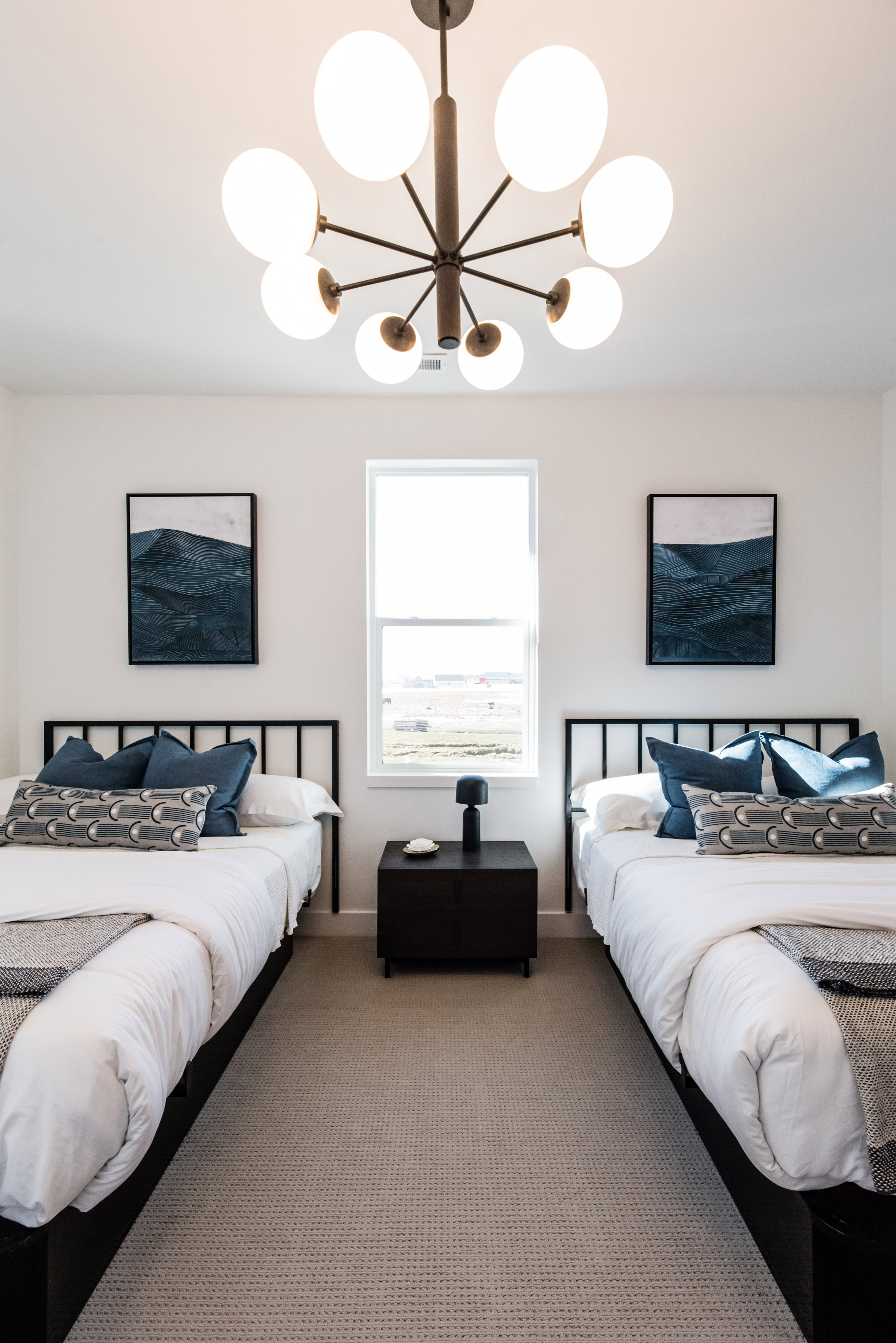 Carpeted bedroom featuring a central window, white walls, and a modern chandelier