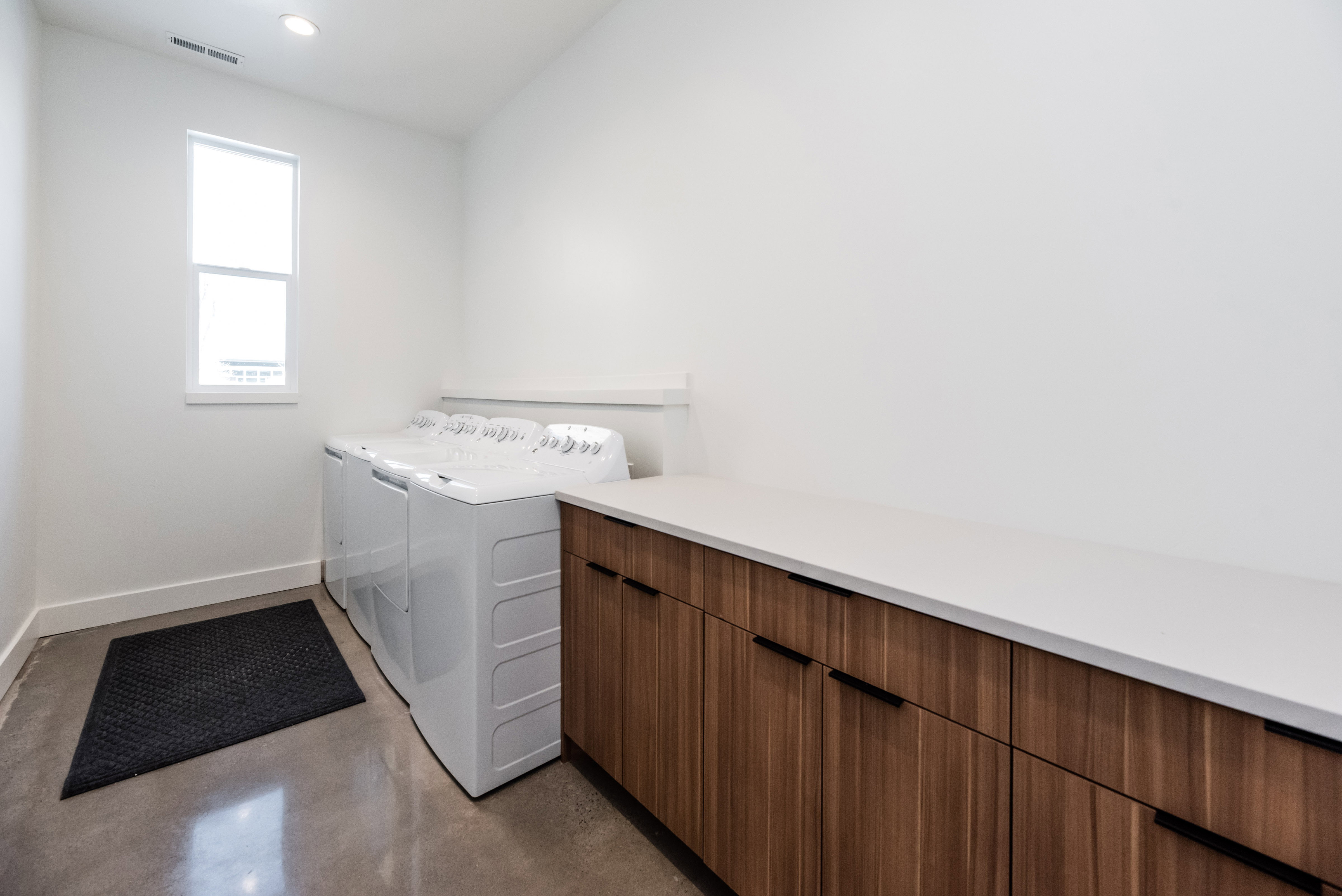 Laundry area featuring wood-finish cabinetry, a light-toned countertop, and concrete flooring