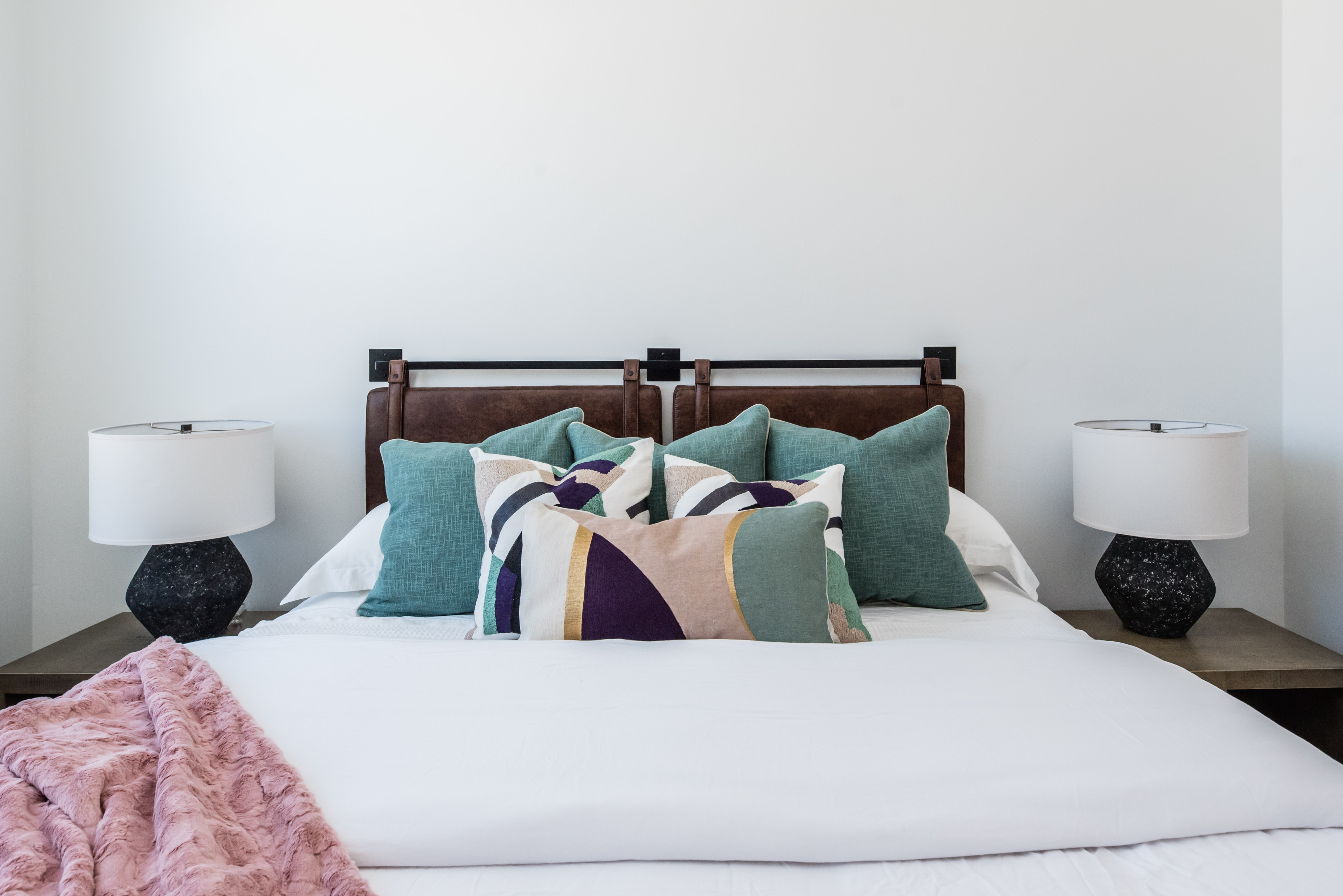 White walls frame a bed featuring a brown leather headboard with black metal accents