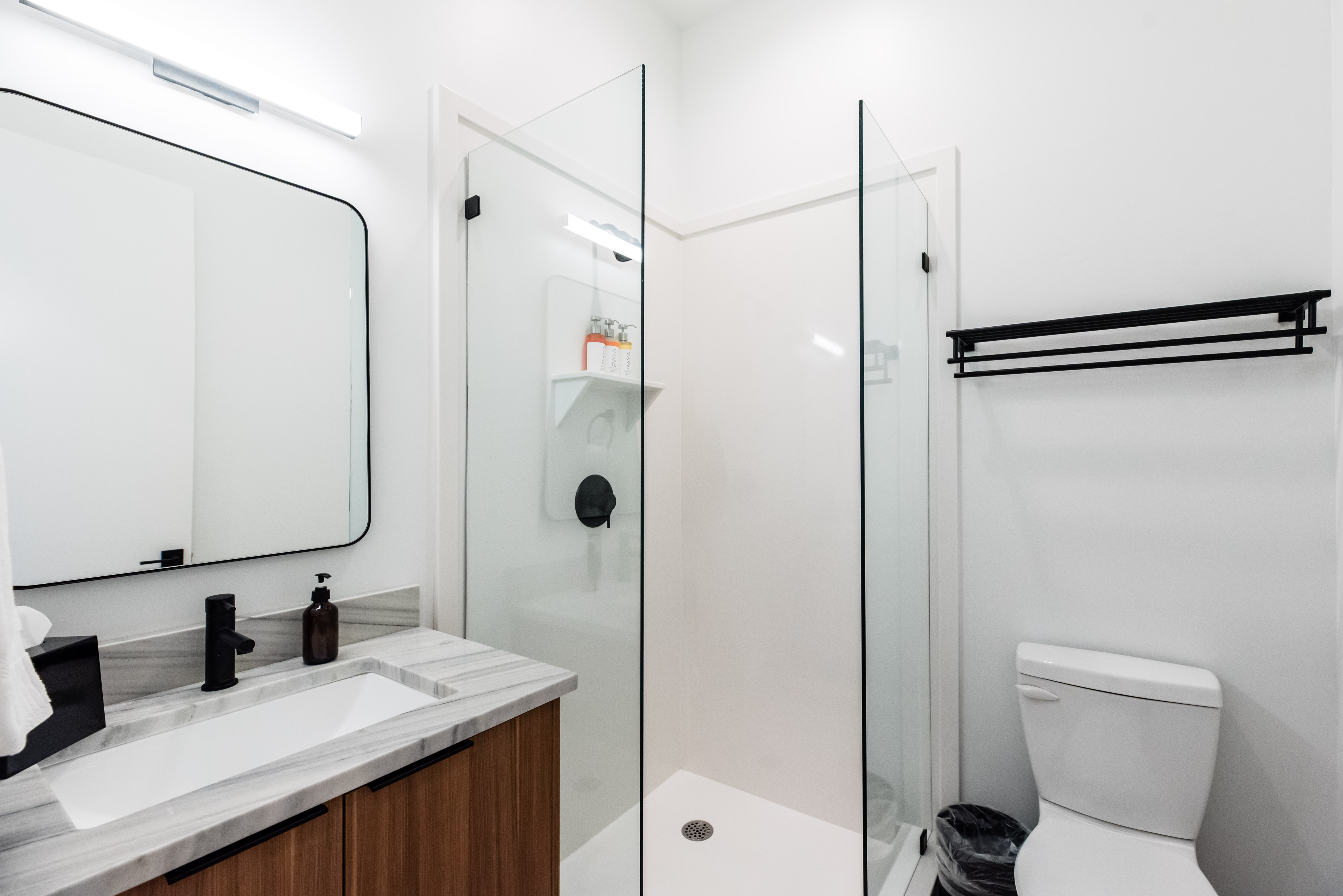Contemporary bathroom featuring a glass-enclosed shower with matte black fixtures, a wood-finish vanity with a rectangular undermount sink, a stone-patterned countertop, and a modern rectangular mirror with a black frame