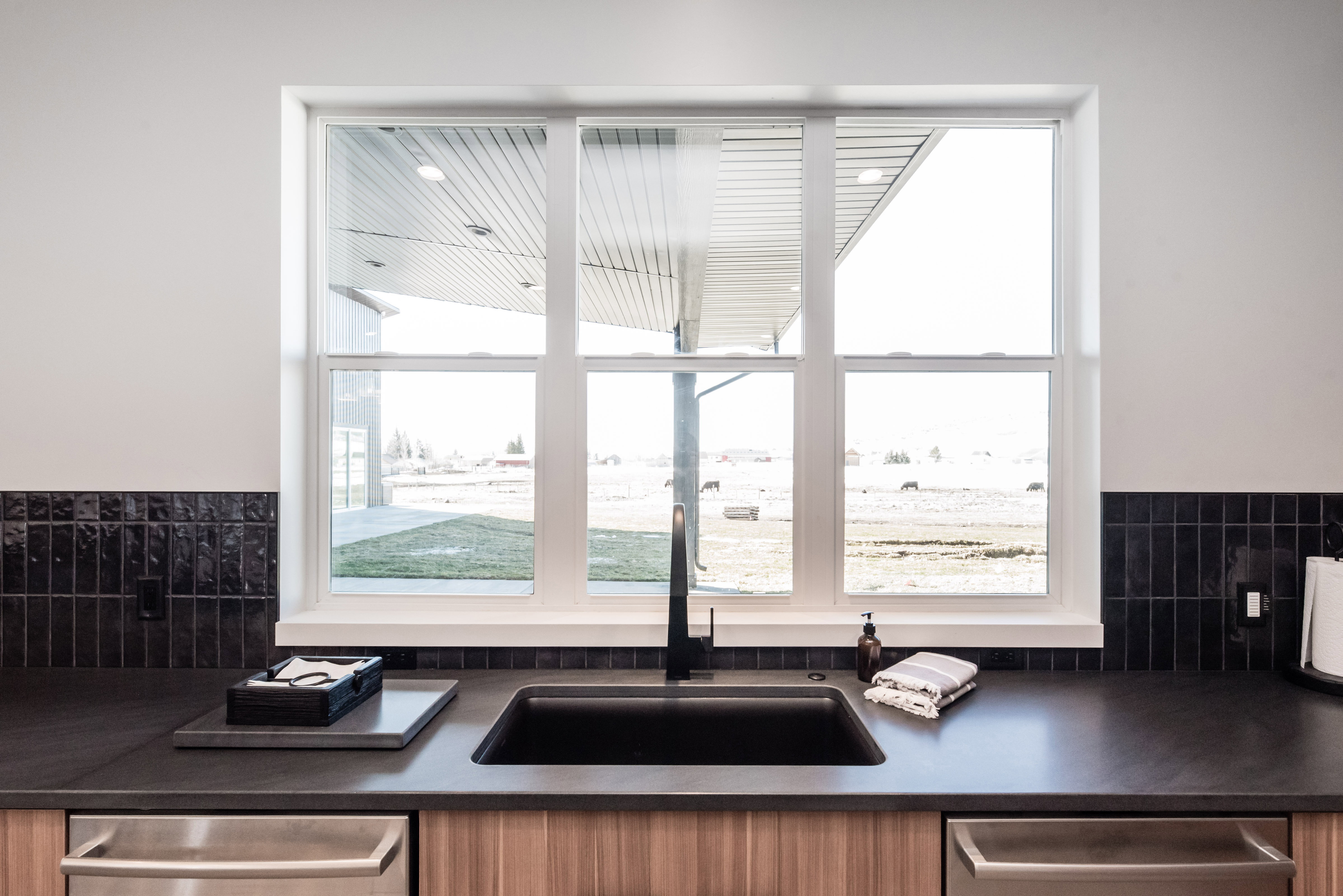 Kitchen features a triple-pane window, dark solid surface countertops, a black undermount sink with a matte black faucet, and a black subway tile backsplash