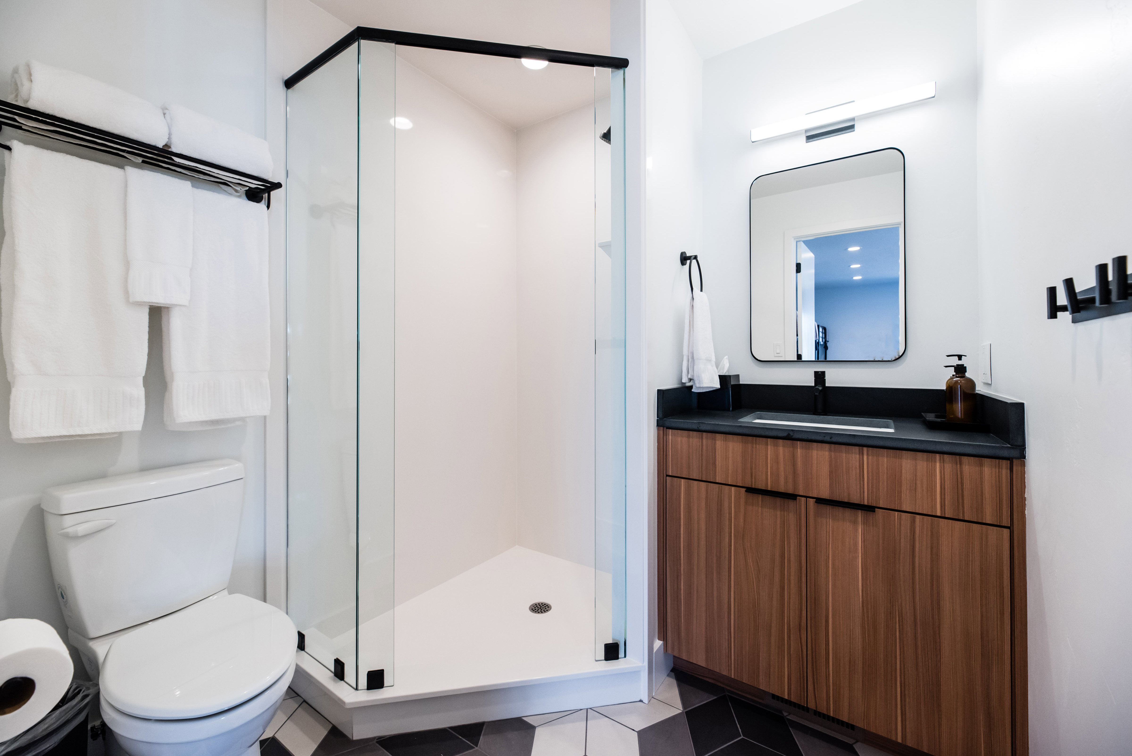 Bathroom featuring a corner glass-enclosed shower with black trim, a wood-finish vanity with a dark countertop and integrated sink, a rectangular framed mirror, and a white toilet