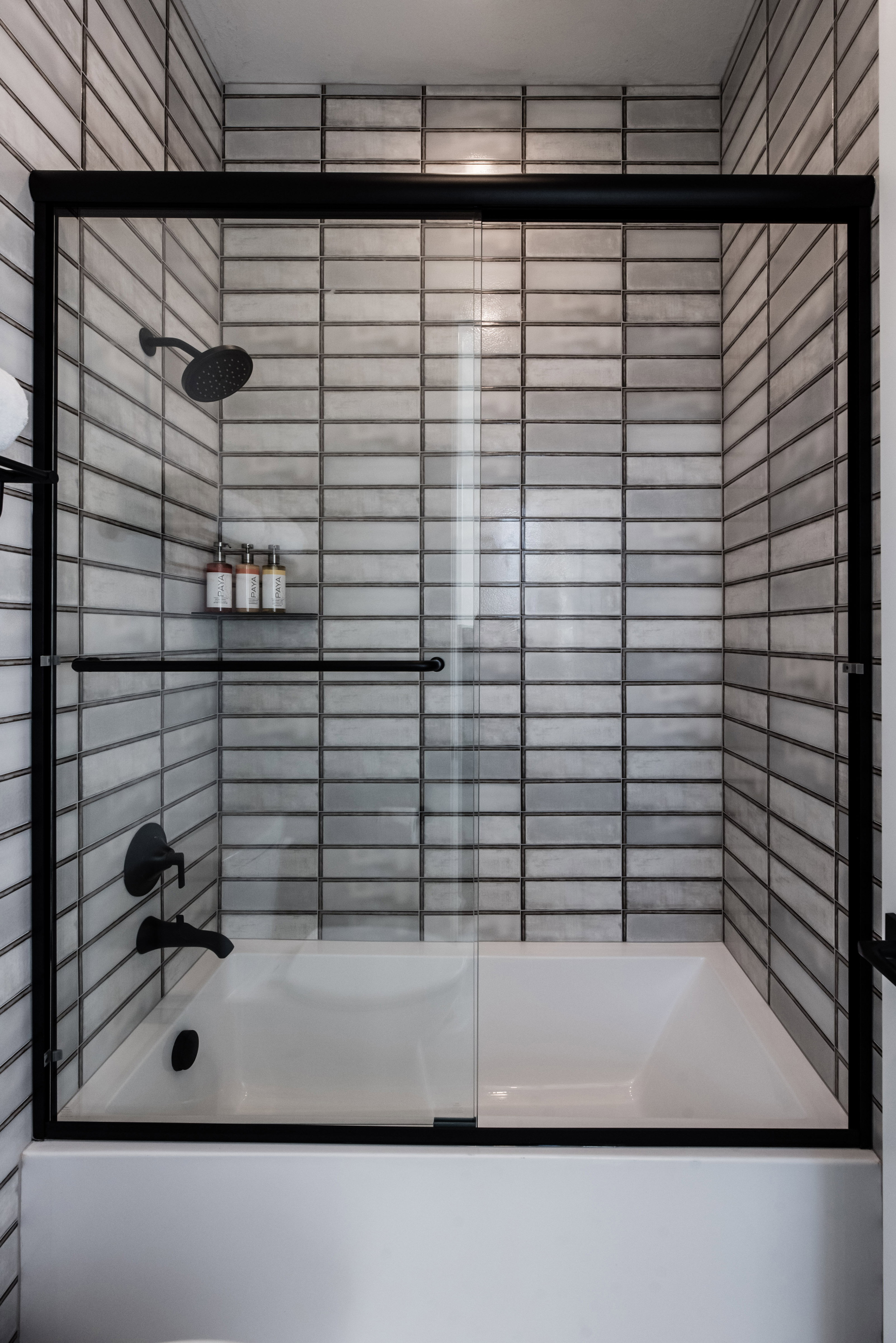 Bathtub with a black-framed glass enclosure, subway tile surround, and matte black fixtures