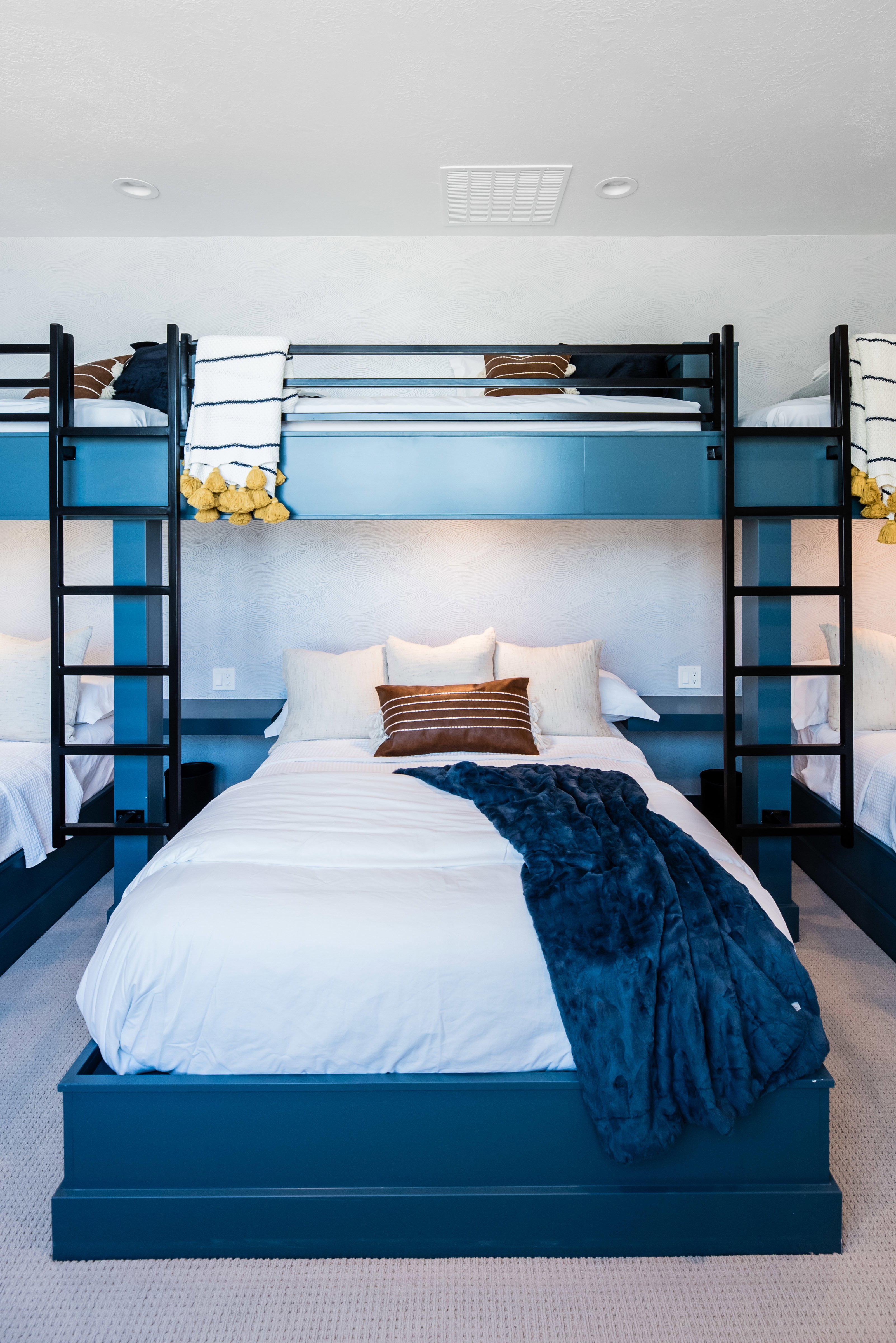 Bedroom featuring three built-in bunk beds with integrated ladders, white textured walls, recessed lighting, and a neutral carpeted floor