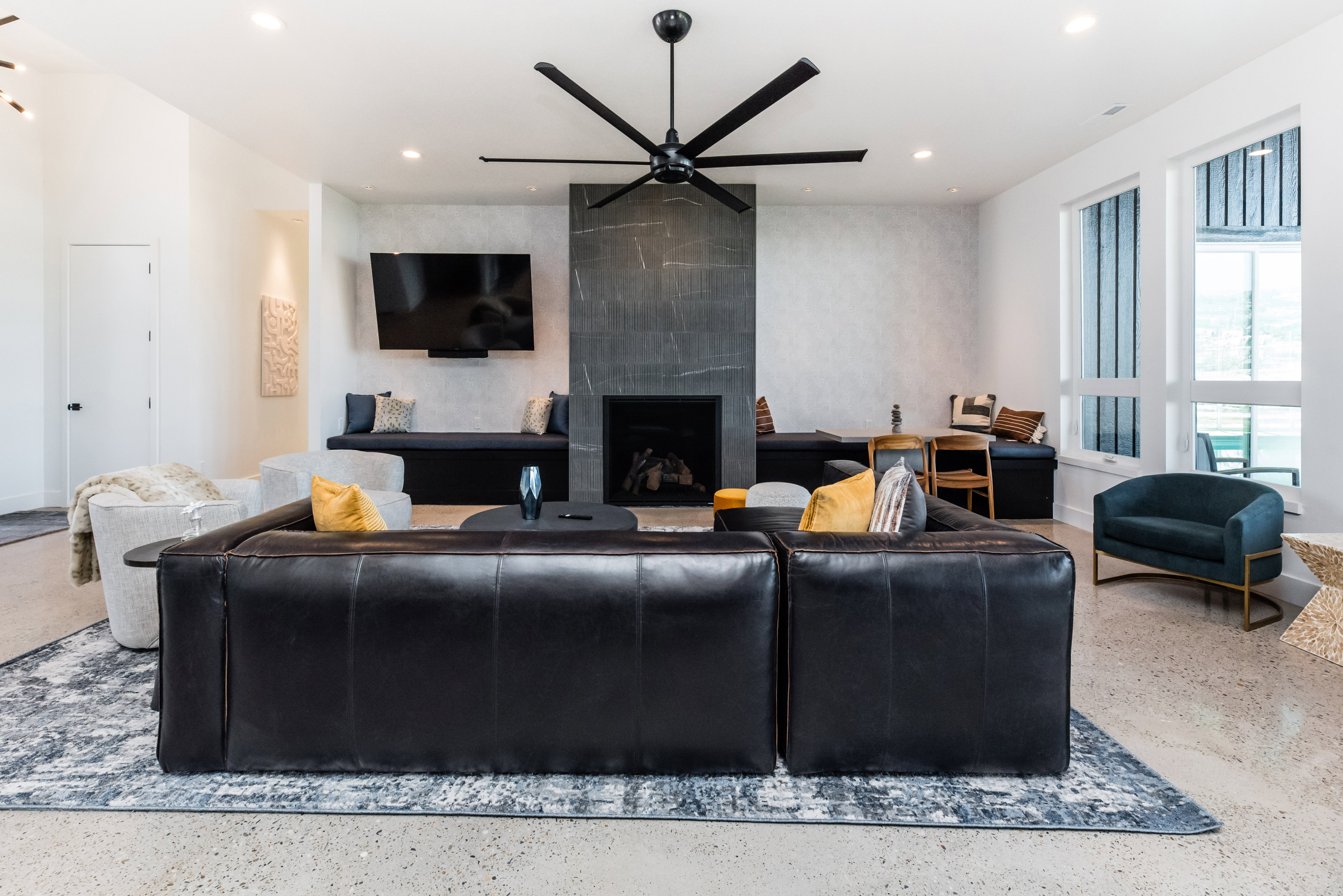 Open-concept living space with polished concrete flooring, a modern linear fireplace with a stone surround, and a ceiling-mounted fan