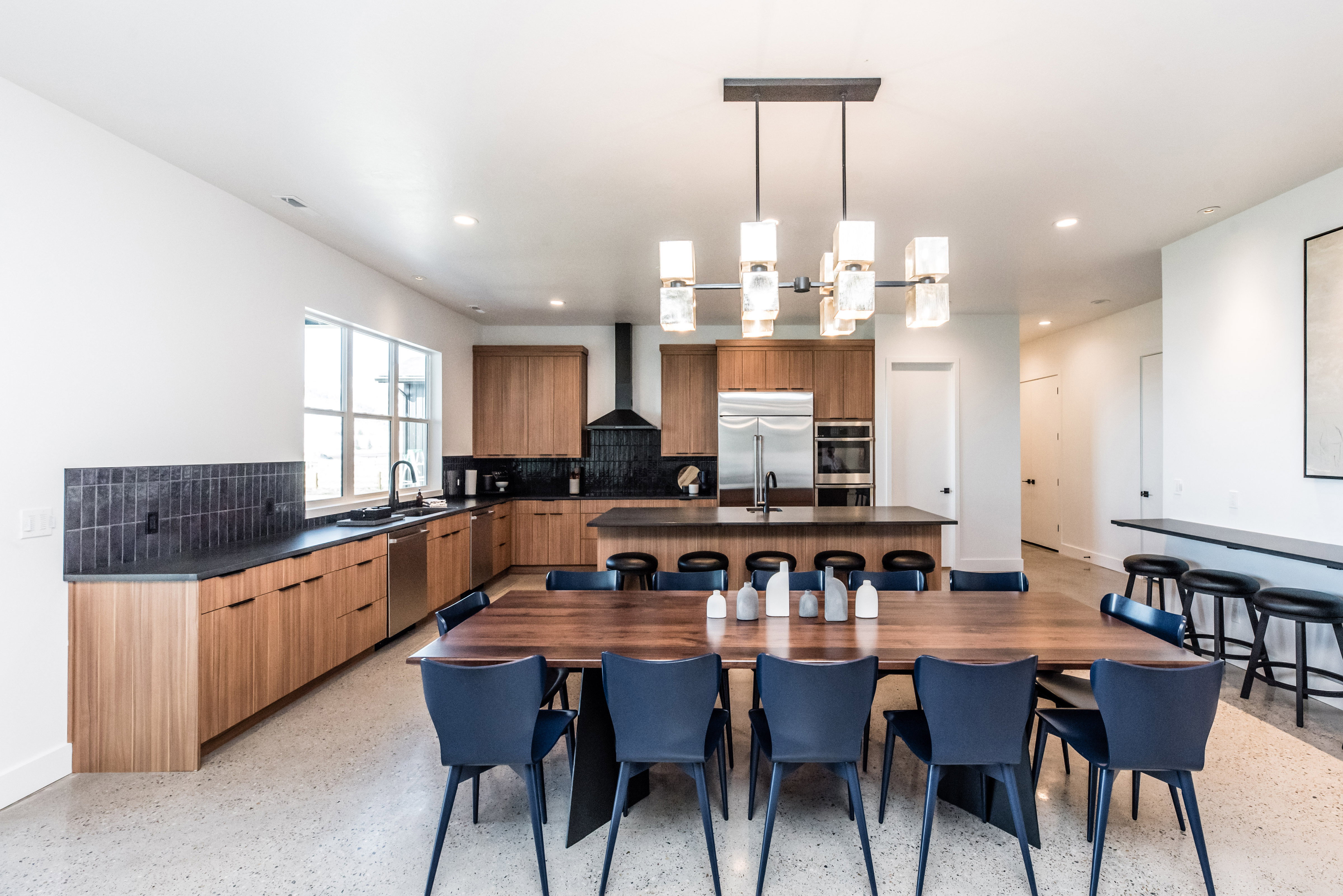 Open-concept kitchen and dining area featuring light wood-finish cabinetry, dark countertops, and a black tile backsplash