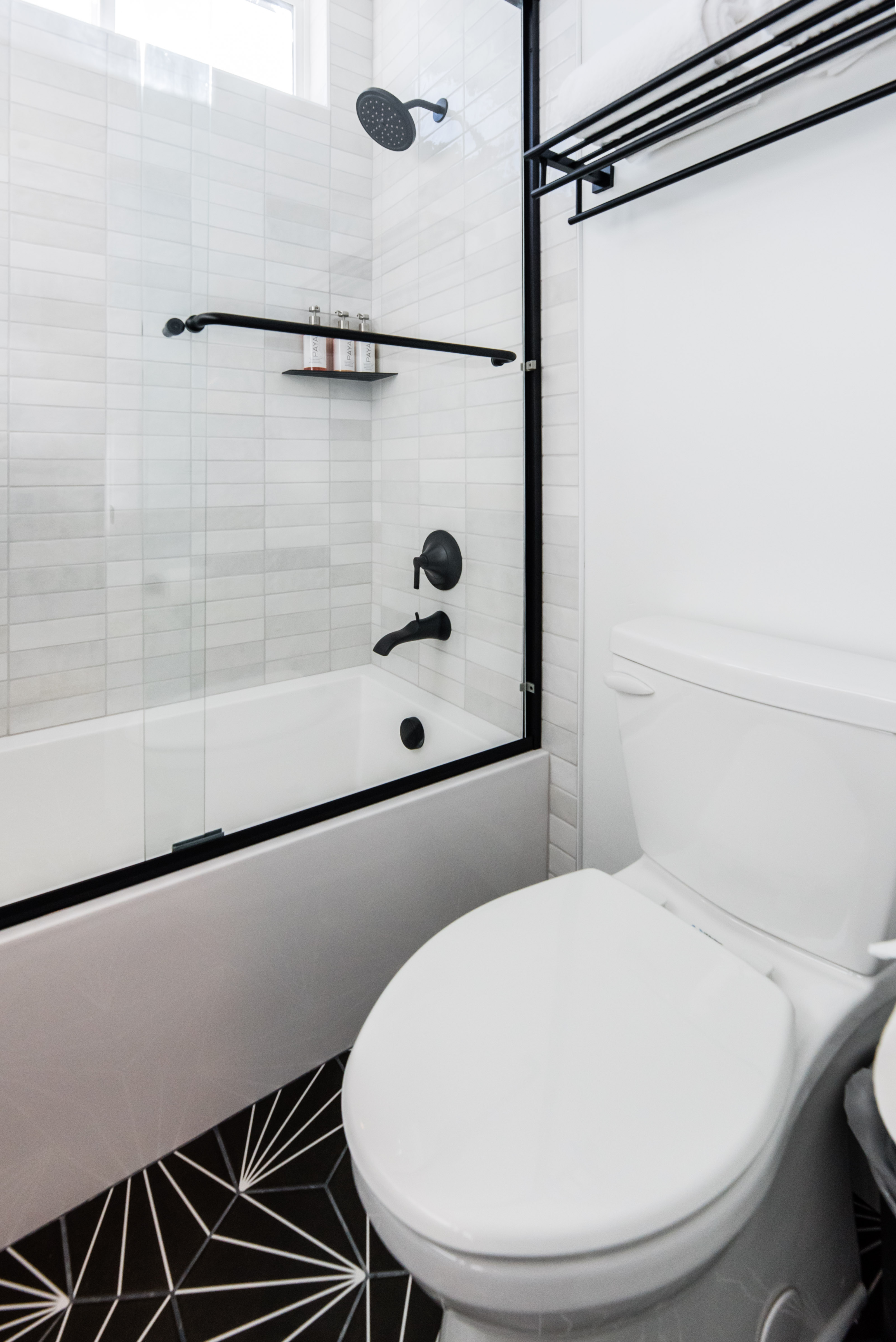 Bathroom featuring a shower-tub combination with black-framed glass enclosure, matte black fixtures, white subway tile surround, and a geometric pattern floor tile