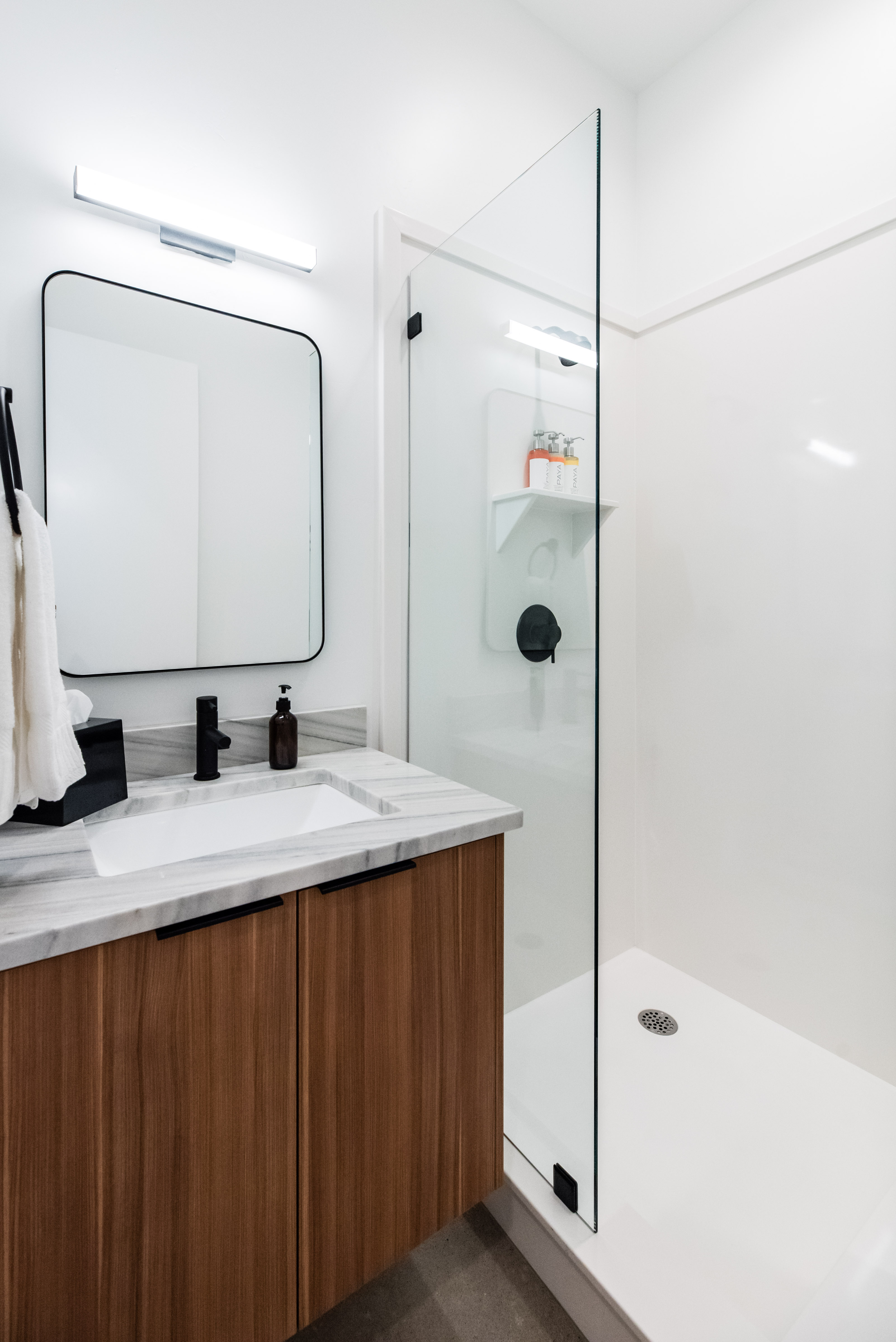 Bathroom featuring a wood-finish vanity with a light-toned countertop, an undermount sink, and a black-framed mirror
