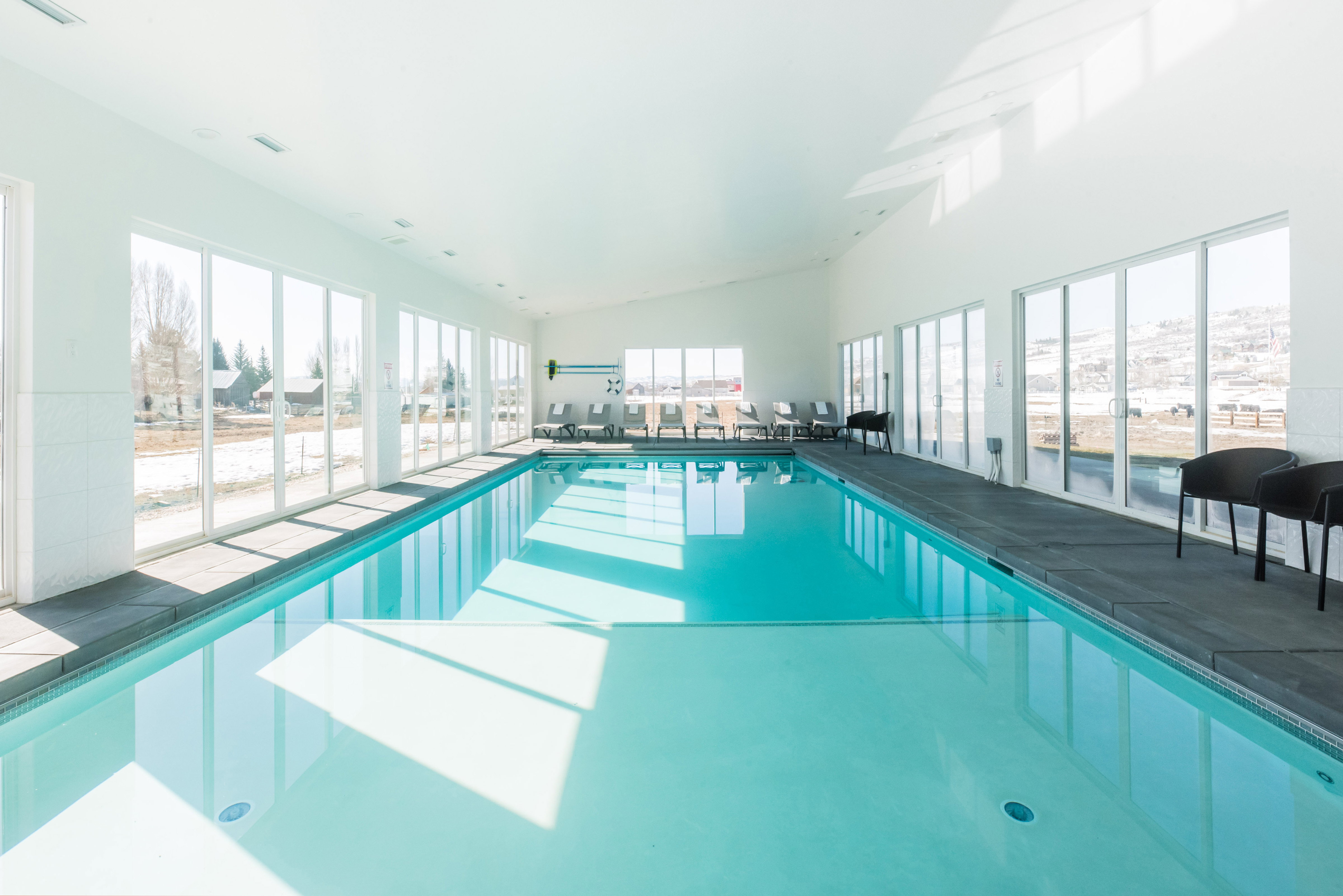 Indoor swimming pool with full-height windows, a white ceiling, and dark-toned coping