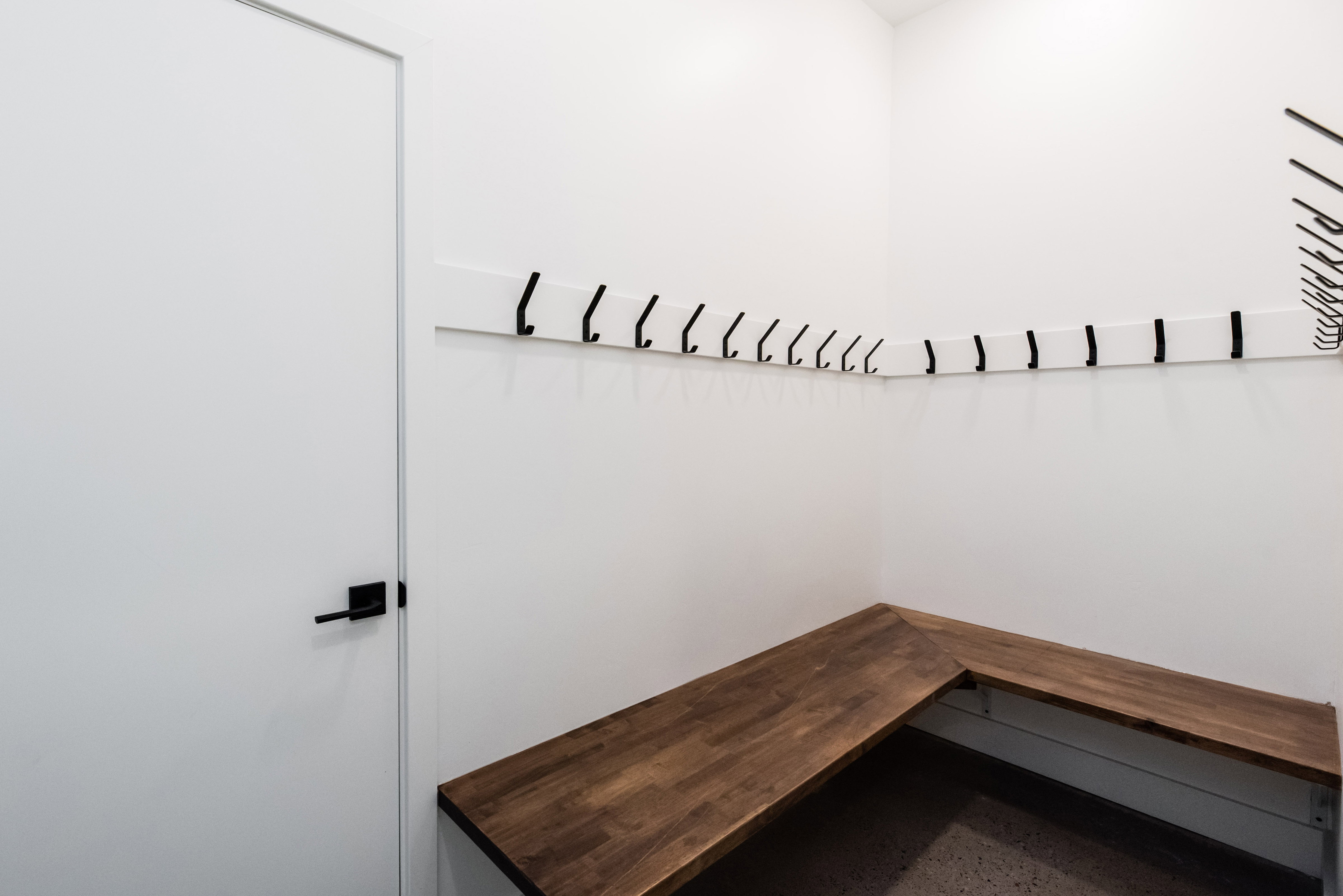 Built-in corner bench with wood-finish top and white walls featuring multiple coat hooks