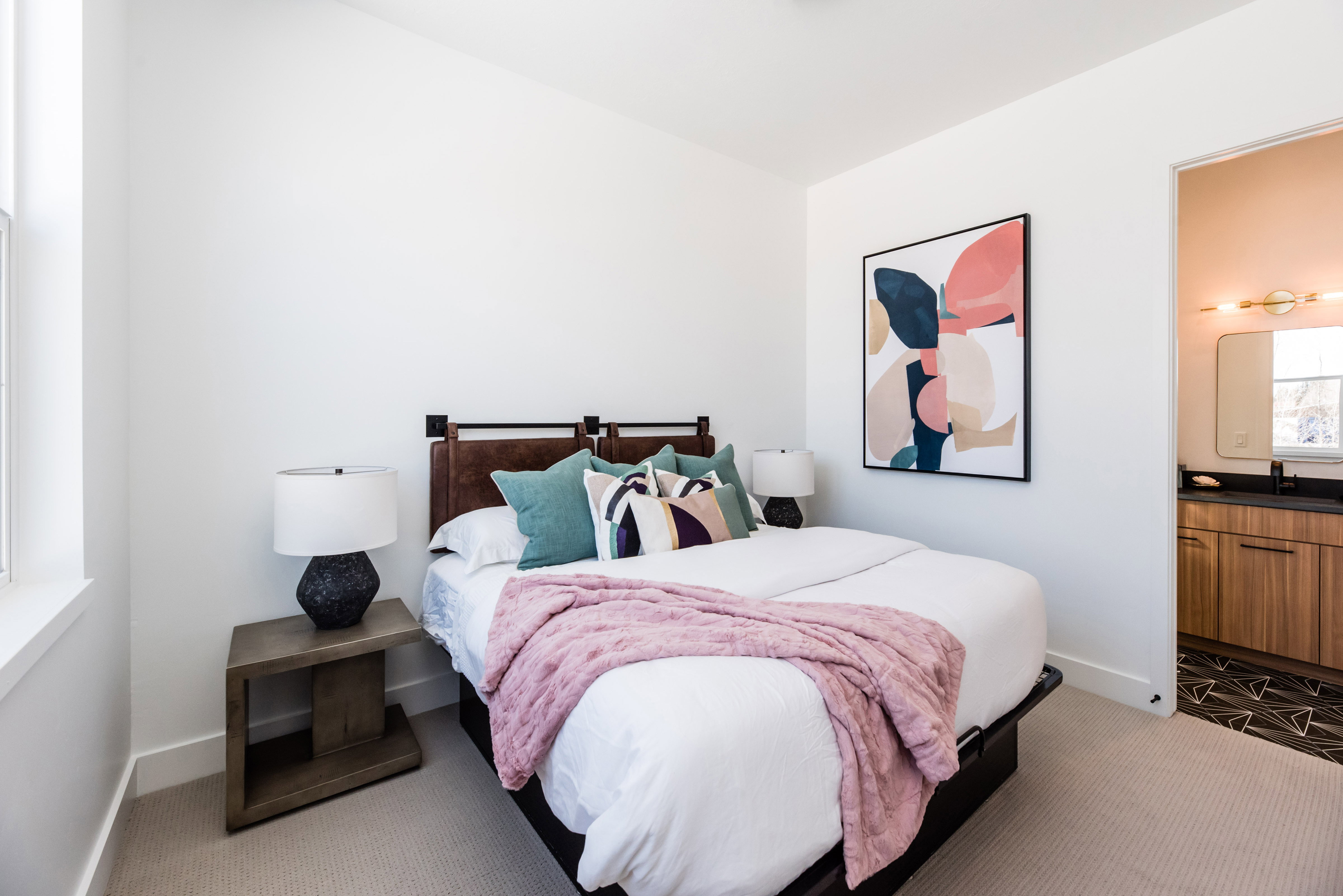 Bedroom featuring light-toned carpeting, a window with white trim, and a doorway opening to a bathroom