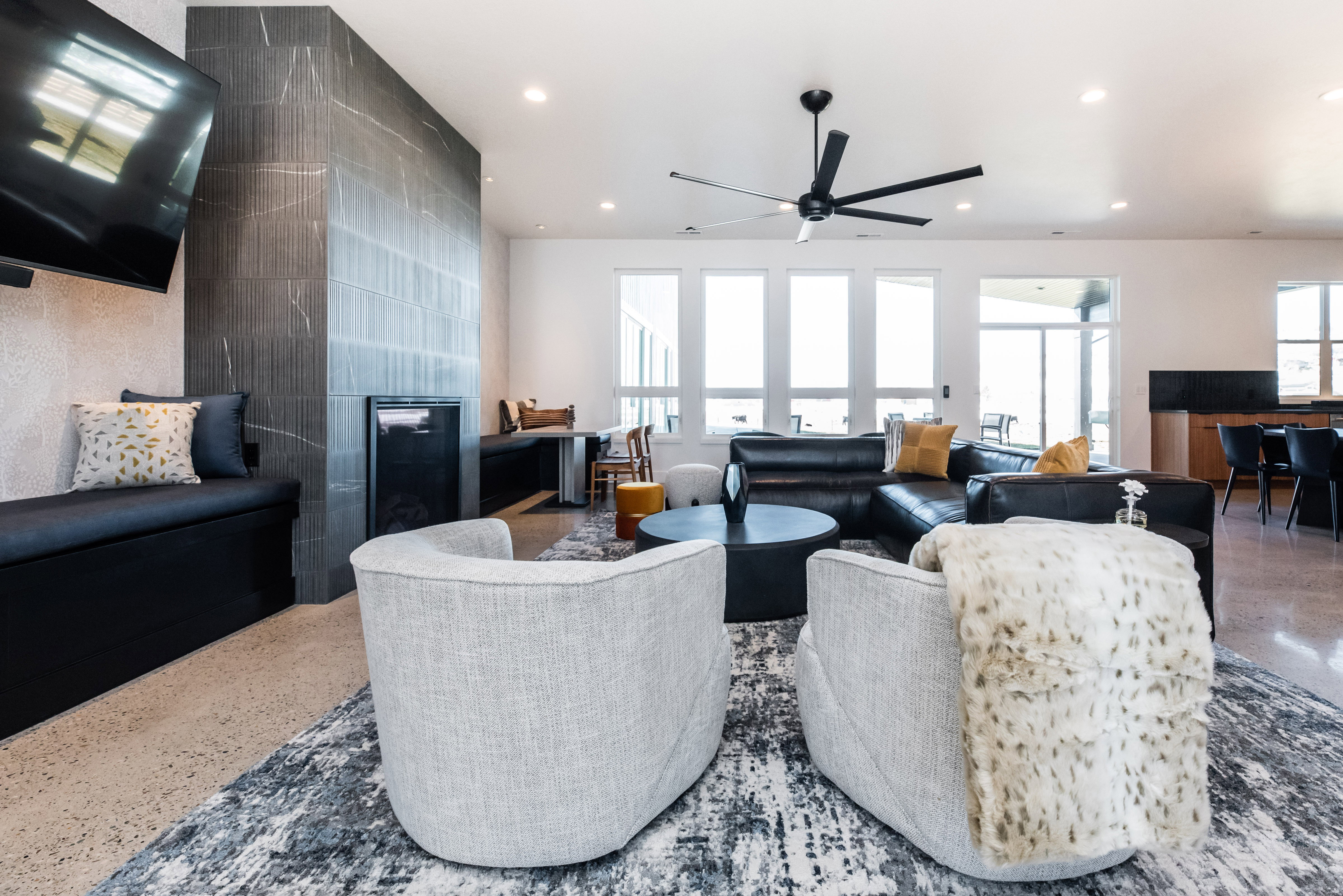 Spacious living area featuring a sleek fireplace with dark-toned tile surround, built-in window seating, multiple large windows, a modern ceiling fan, and recessed lighting