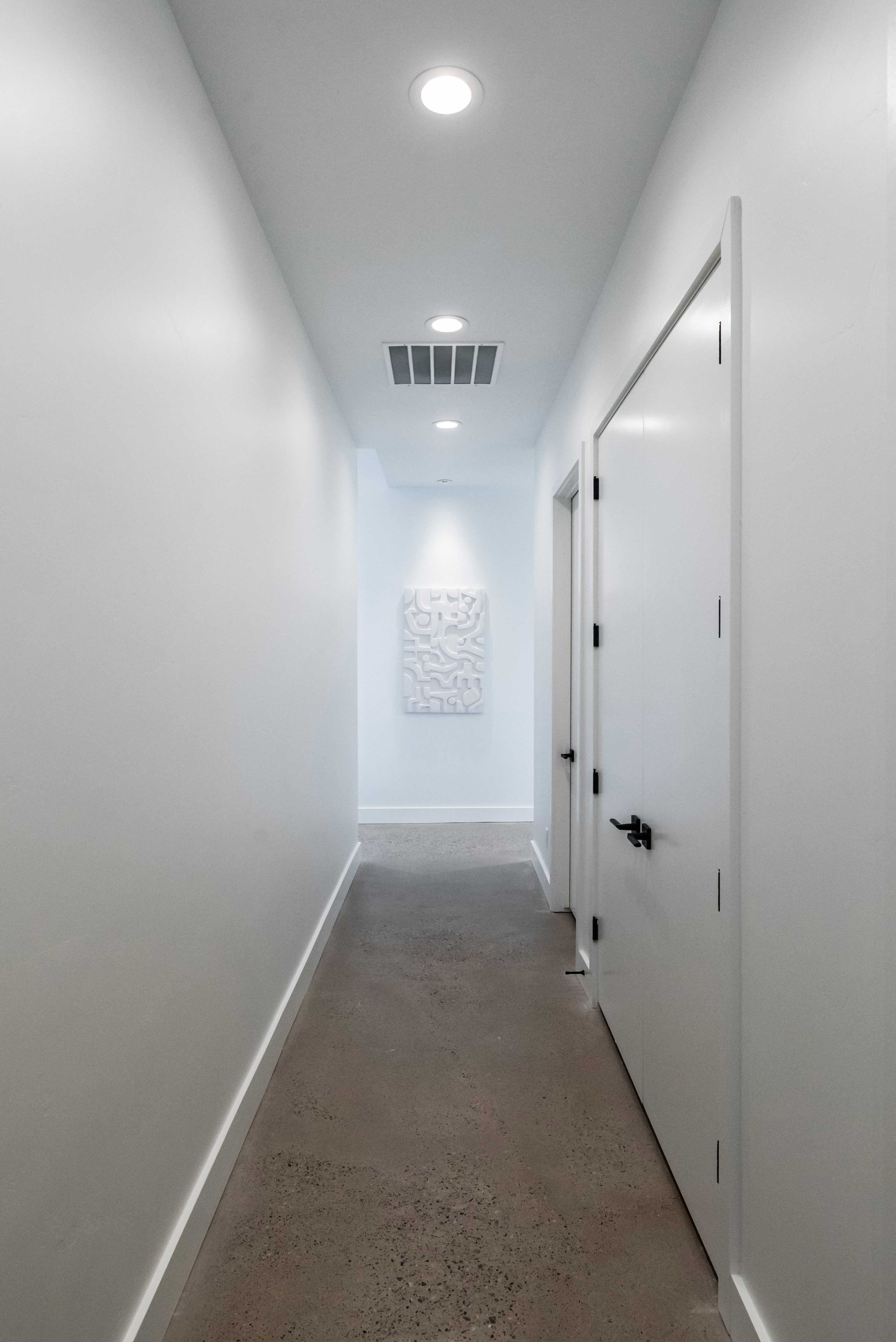 Modern interior corridor featuring recessed ceiling lighting, a white painted finish, and a textured wall art piece