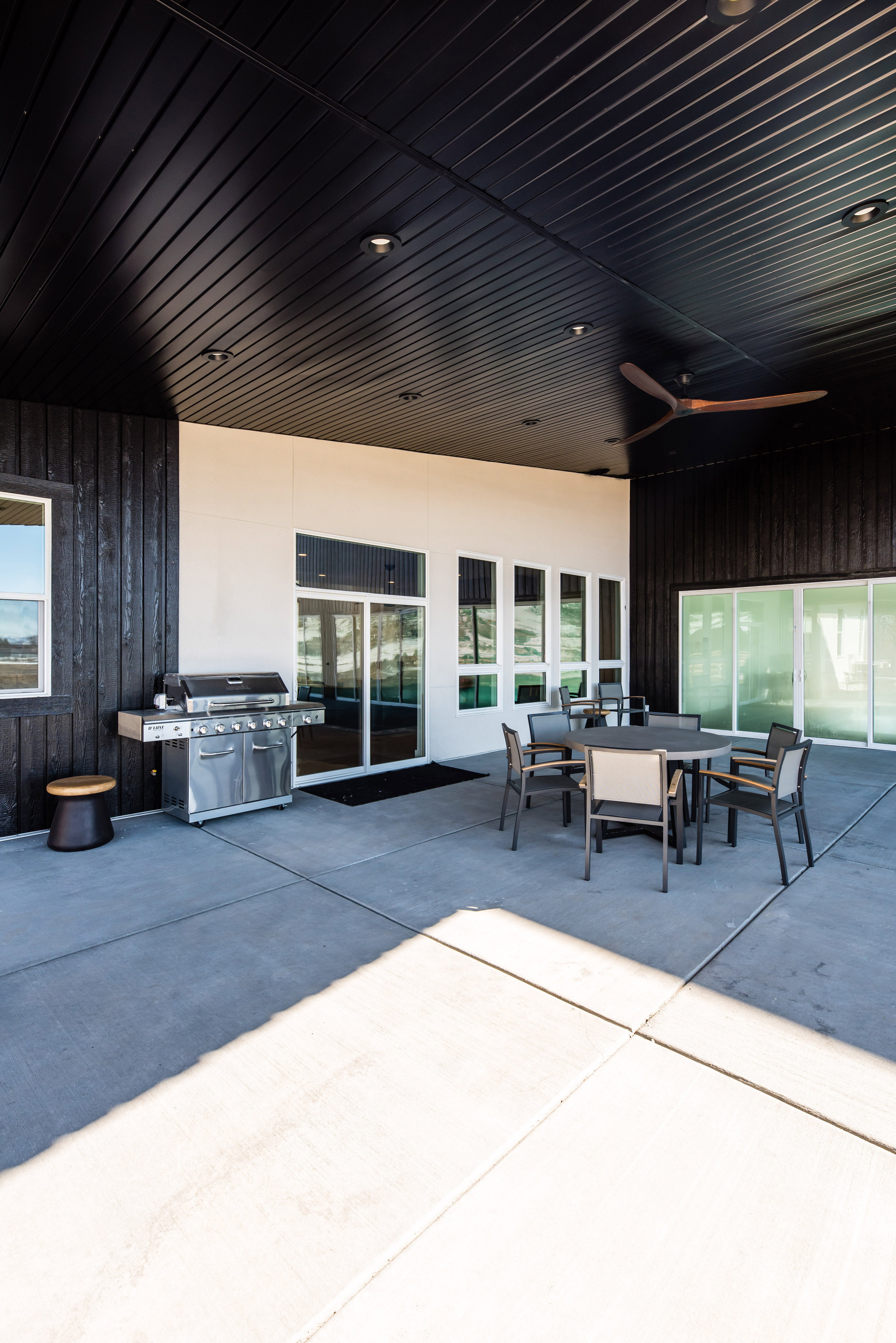 Expansive outdoor patio featuring a concrete surface, a black slatted ceiling with recessed lighting, and a modern ceiling fan