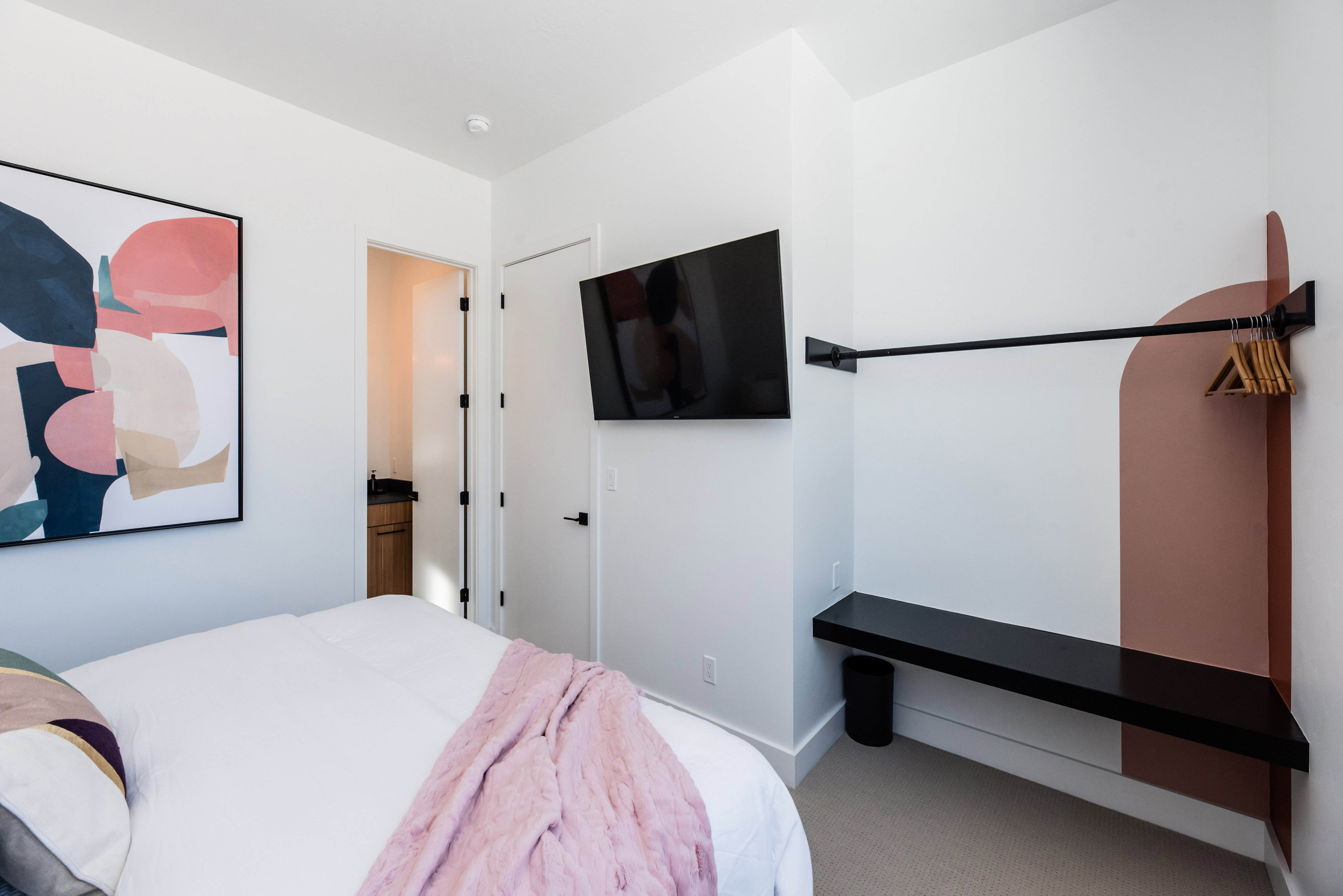 Bedroom featuring a wall-mounted television, a built-in hanging rod, and a floating corner shelf