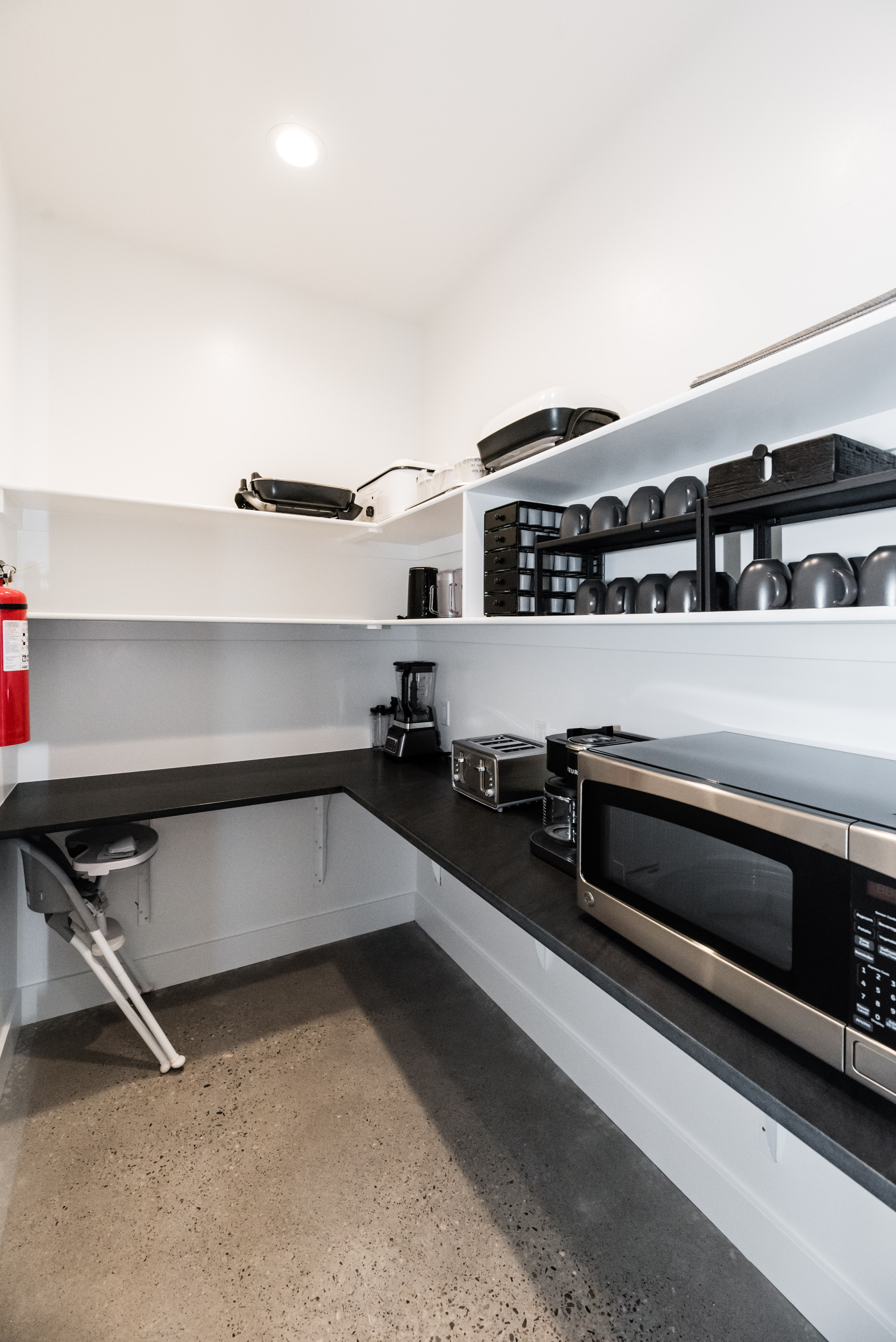 Spacious walk-in pantry featuring concrete flooring, a corner countertop with an integrated basin, and multiple levels of built-in shelving